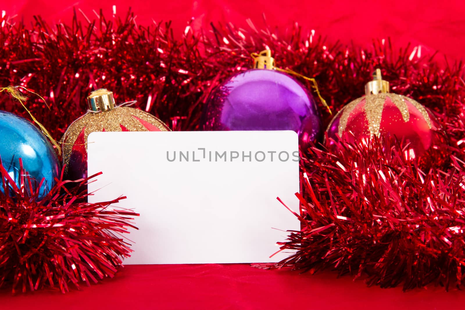 Blank greeting card for your message and xmas ornaments with colorful balls on red fabric.