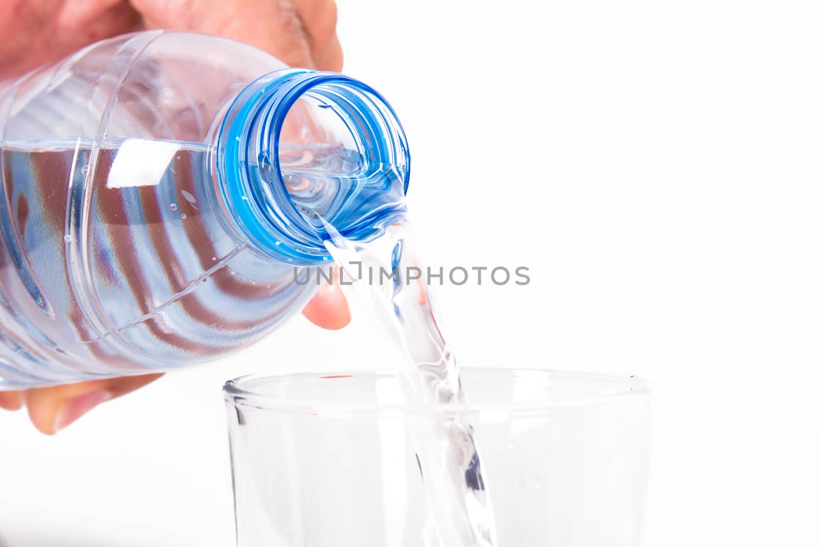 Water pouring into glass from plastic bottle, isolated on white background.
