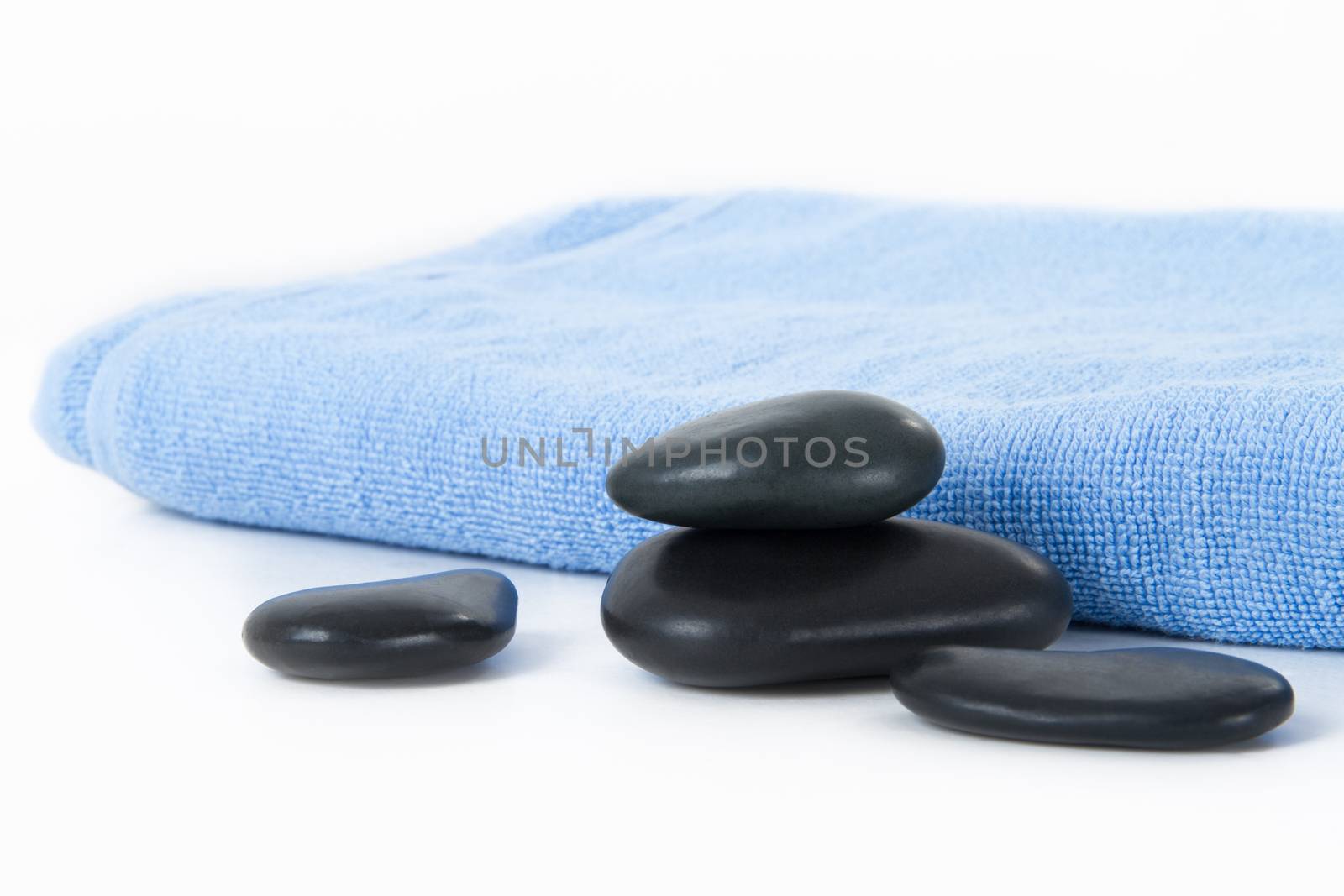 Black massage stones on balance and blue towel, isolated on white background.