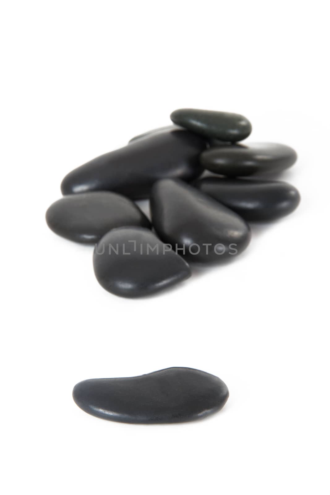 Single black massage stone standing out from the crowd, isolated on white background.