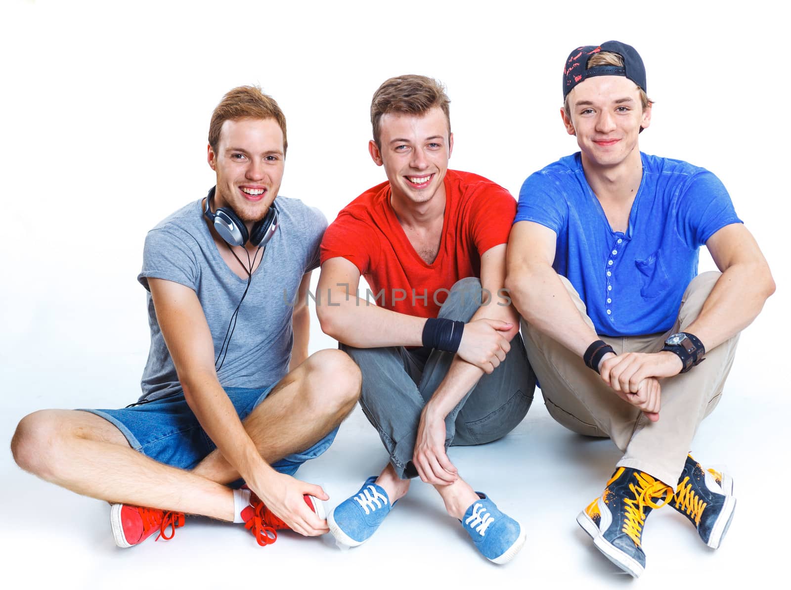 Three young happy smiling teenagers sitting on the floor. Isolated on white background.