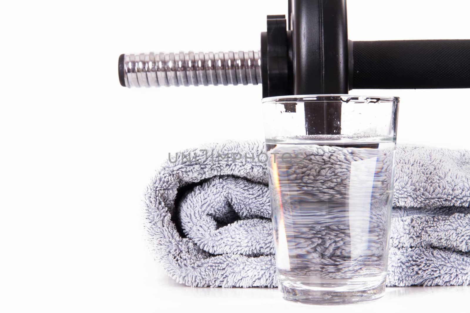 Close up of black gym barbell, dumbbell with disks, glass of clean water and blue towel, isolated on white background.