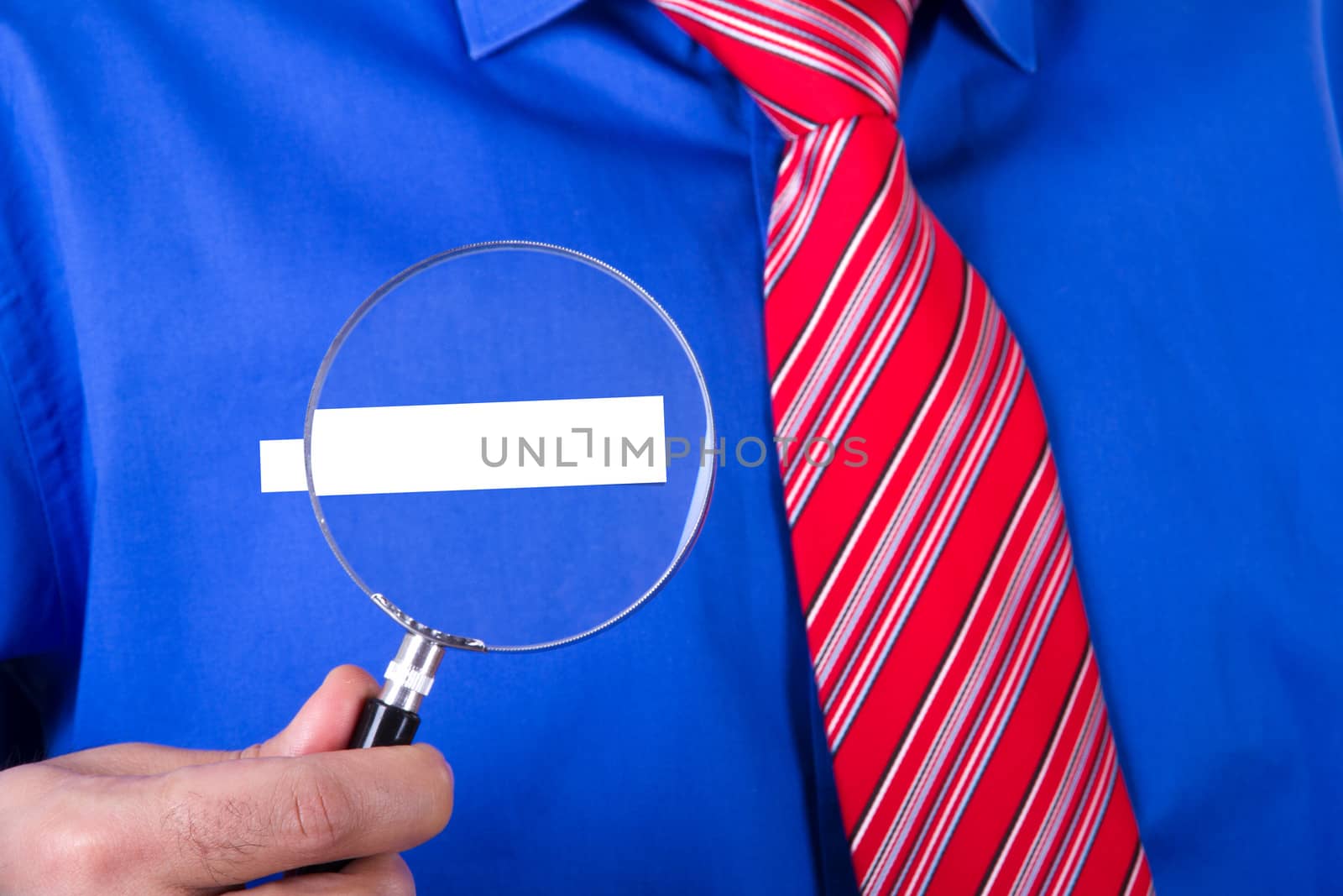 Businessman with red tie and blue shirt showing his blank label title with magnifying glass.