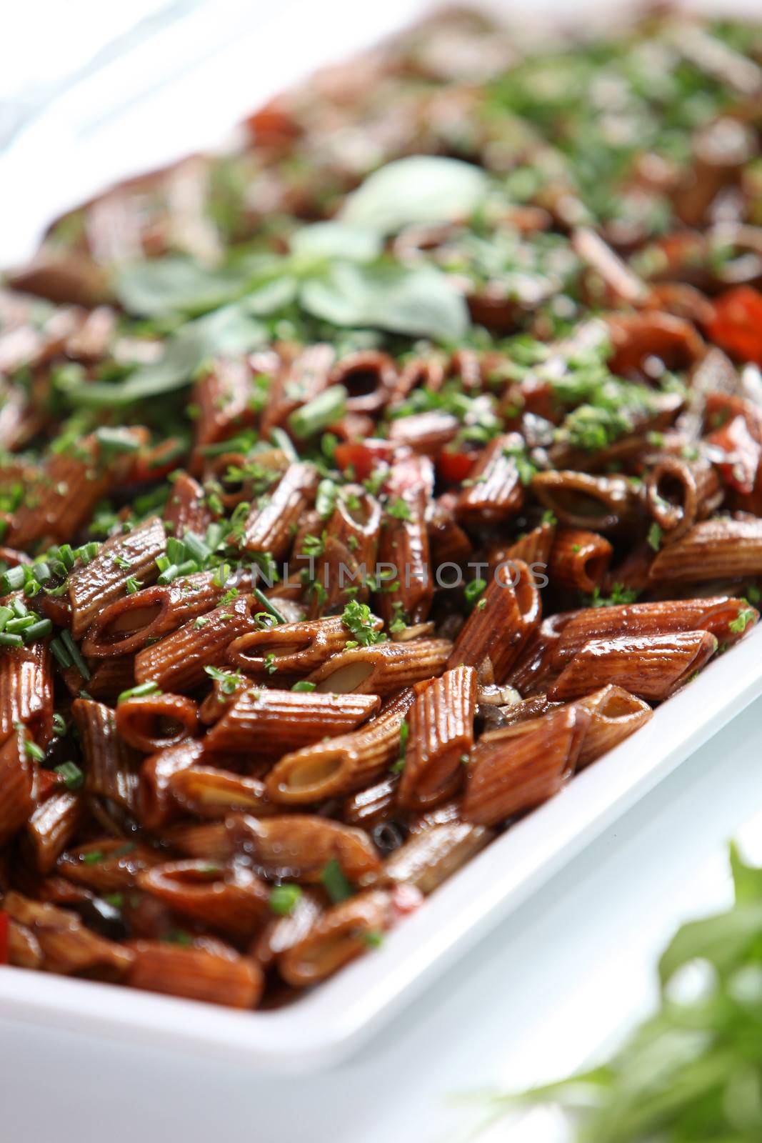 Wholewheat pasta dish with fresh herbs served on a buffet table, close up view with shallow dof