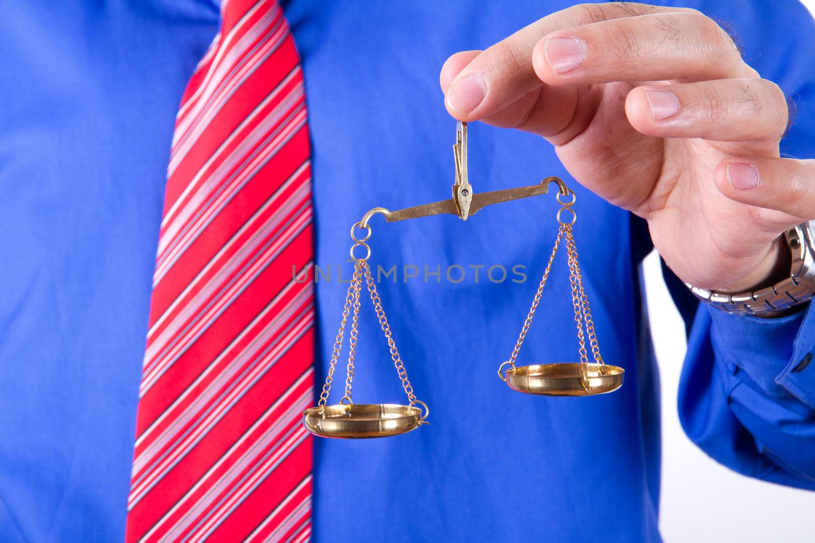 Businessman with red tie and blue shirt holding golden scales unbalanced, isolated on white background.