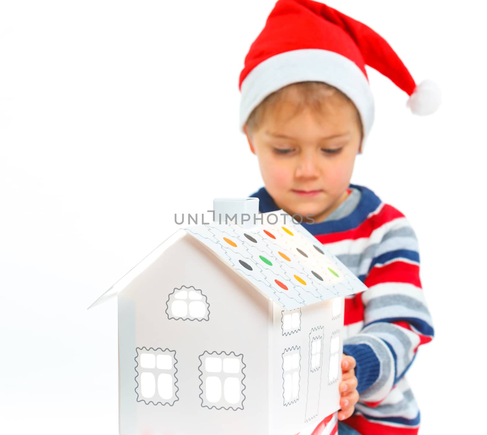 Christmas theme - Smiling boy in Santa's hat with white gingerbread house, isolated on white
