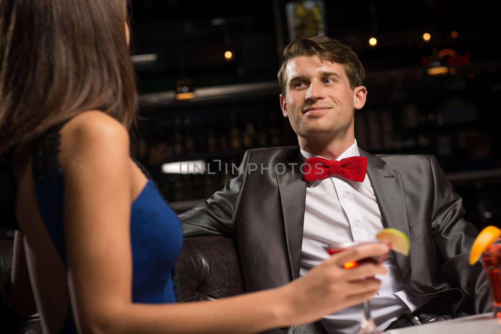 portrait of a man in a nightclub, sitting on the couch and talking with woman