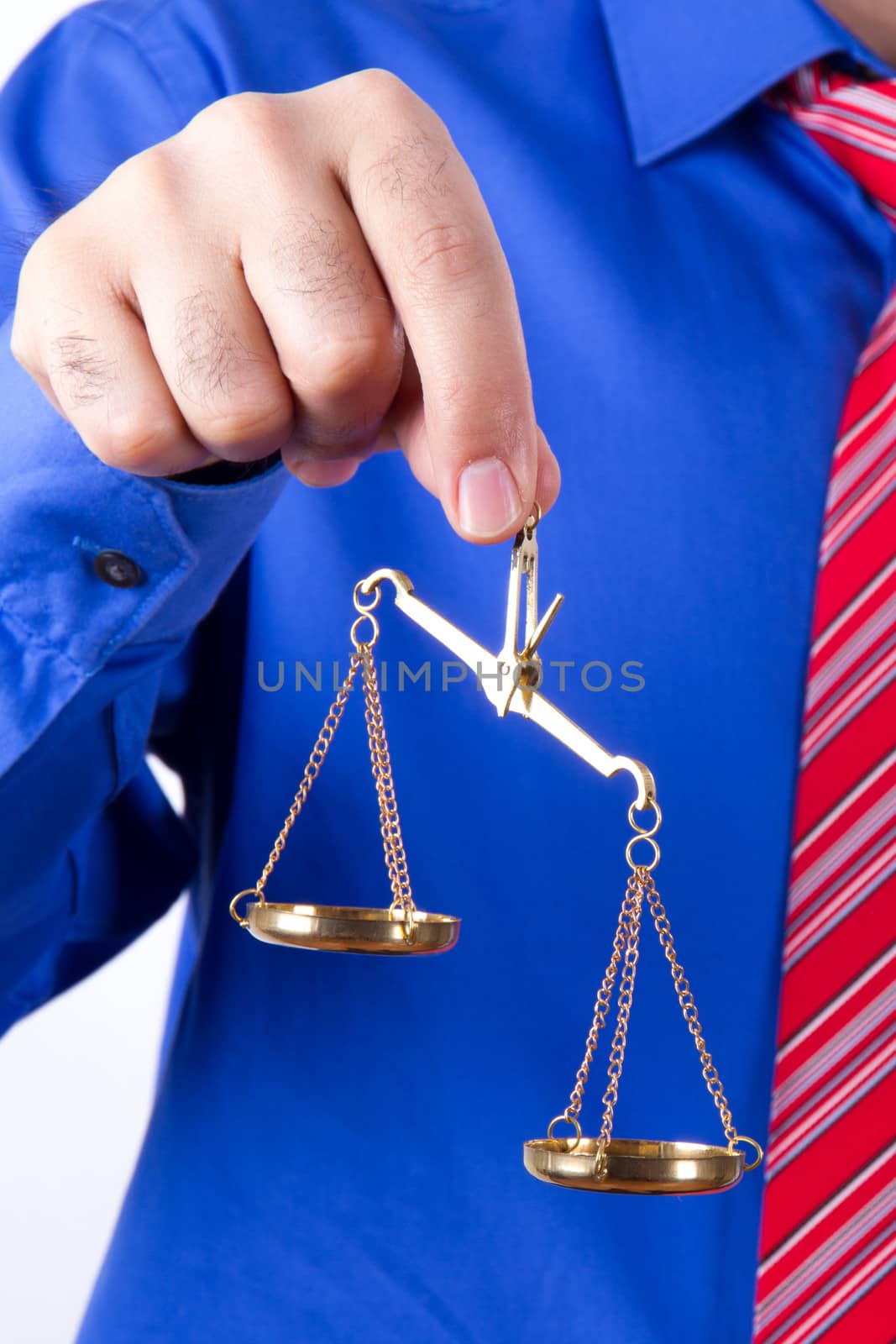 Businessman with red tie and blue shirt holding golden scales unbalanced, isolated on white background.