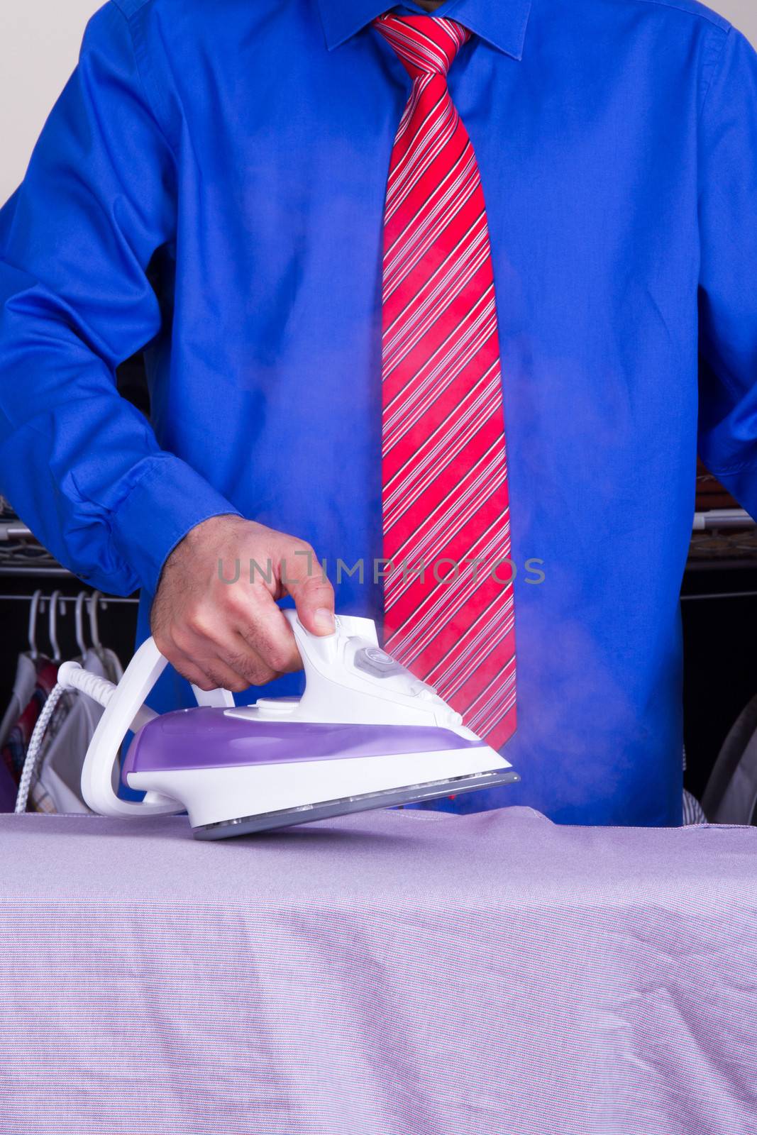 Businessman with red tie and blue shirt ironing against wardrobe.