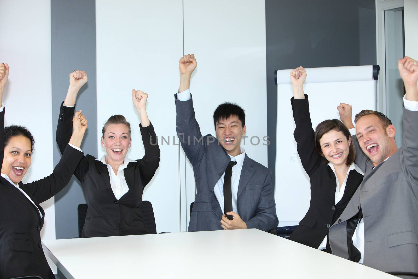 Jubilant successful business team of motivated multiethnic young people sitting celebrating and cheering at a table in the office with broad smiles