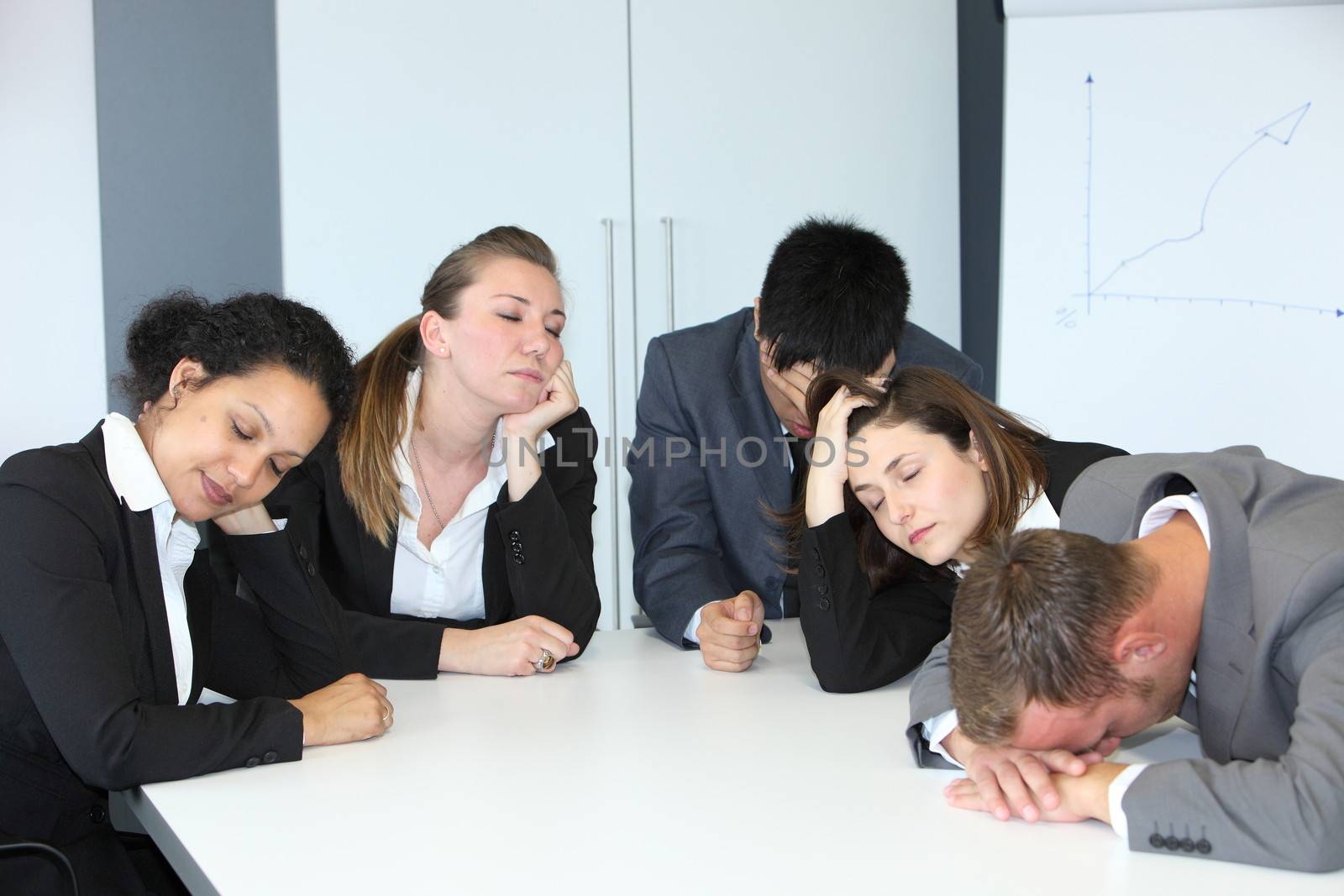 Group of diverse bored demotivated businespeople in a meeting seated at a table n the office napping with their eyes close slouching on the table