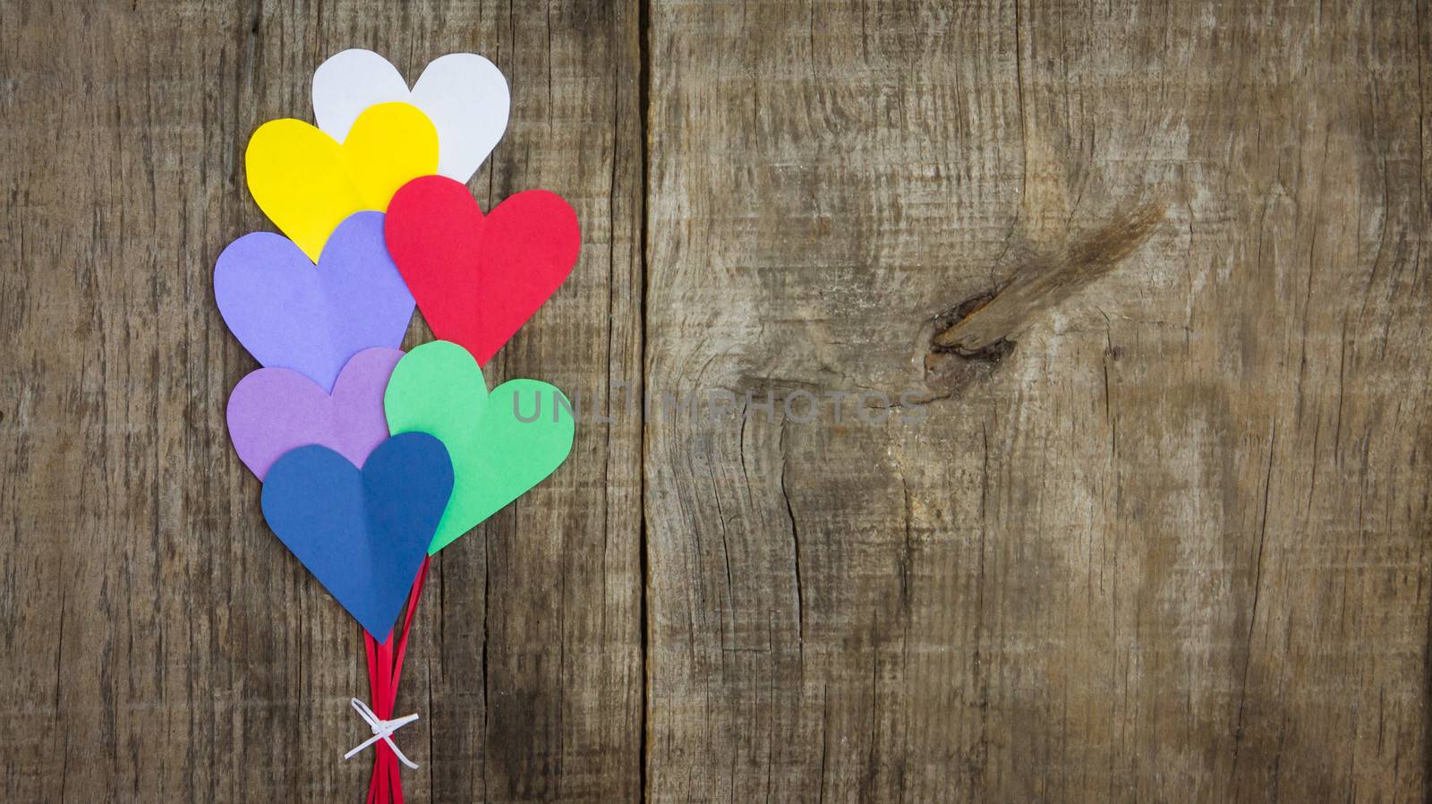 Several colorful paper hearts on wooden textured background