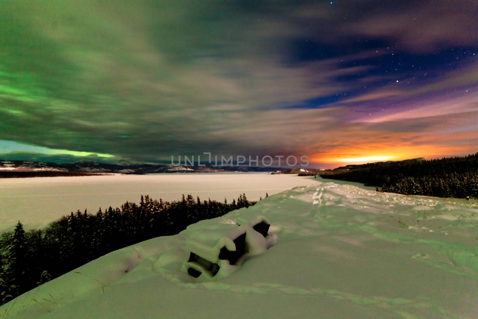 Spectacular view from snow-covered bench: Northern Lights or Aurora borealis clouds and light pollution from the city of Whitehorse over frozen Lake Laberge Yukon Territory Canada winter landscape