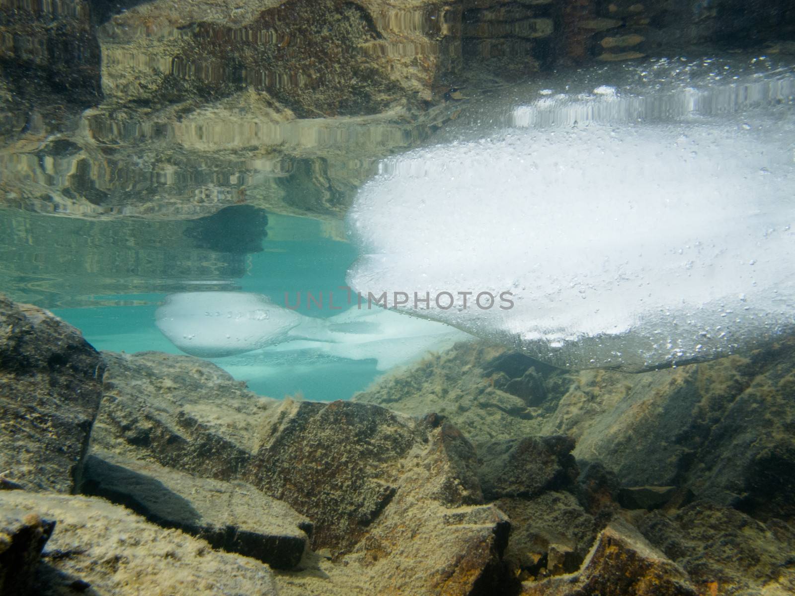 Underwater shot of ice floes floating in clear shallow water with rocky bottom mirrored on water surface
