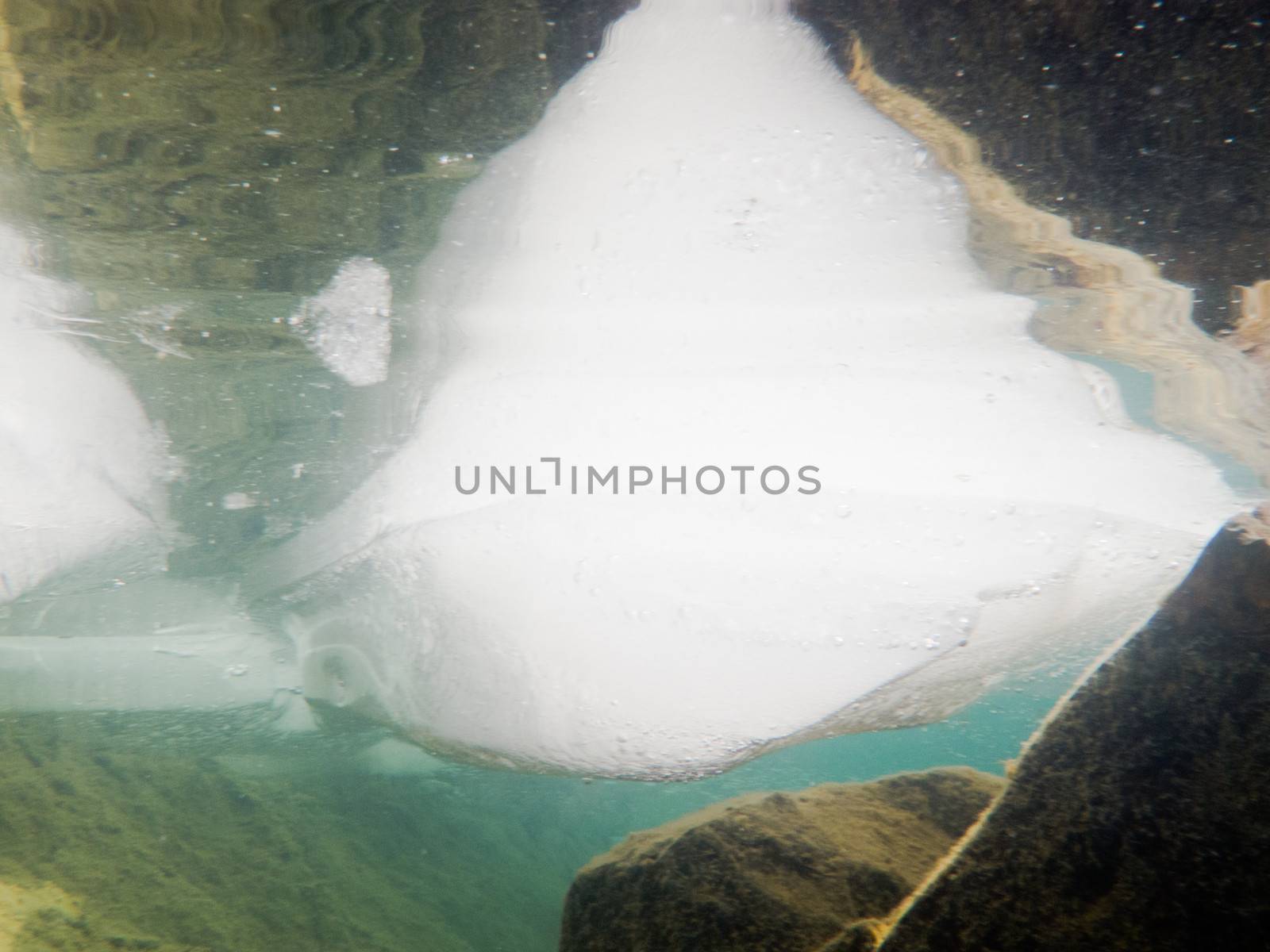 Underwater shot of ice floes floating in clear shallow water with rocky bottom mirrored on water surface