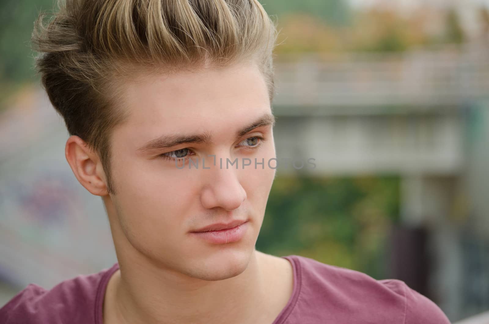 Attractive blue eyed, blond young man's head shot outdoors, looking to a side