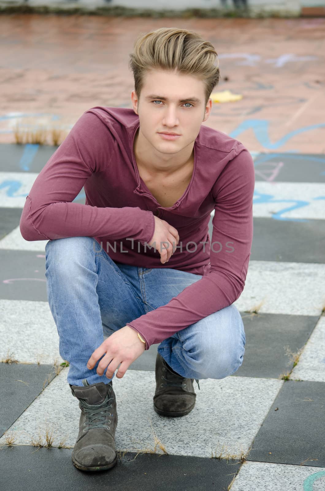 Handsome blond young man, blue eyes, sitting on checkered outdoors floor