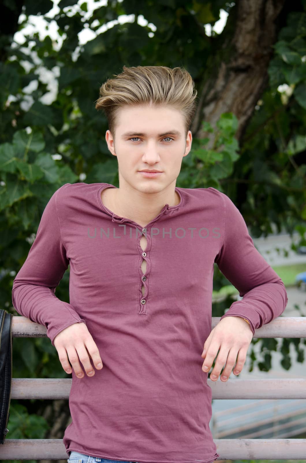 Attractive blue eyed, blond young man leaning on metal railing outdoors