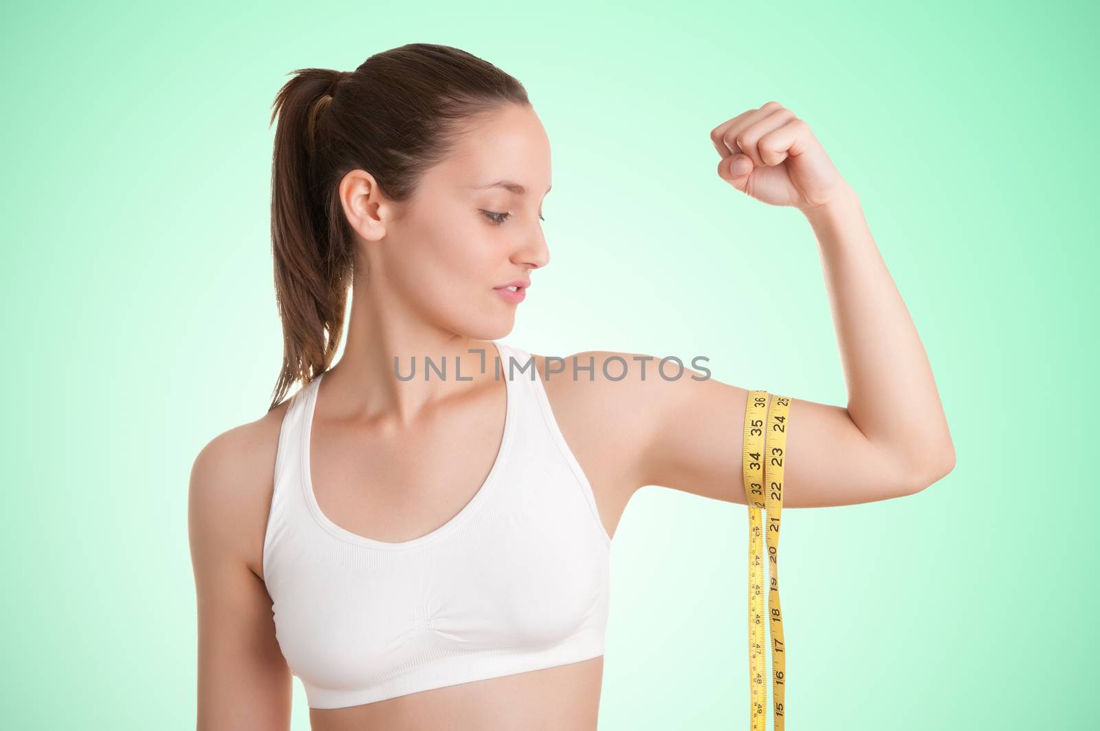 Powerful woman measuring her biceps with a yellow measuring tape in a green background