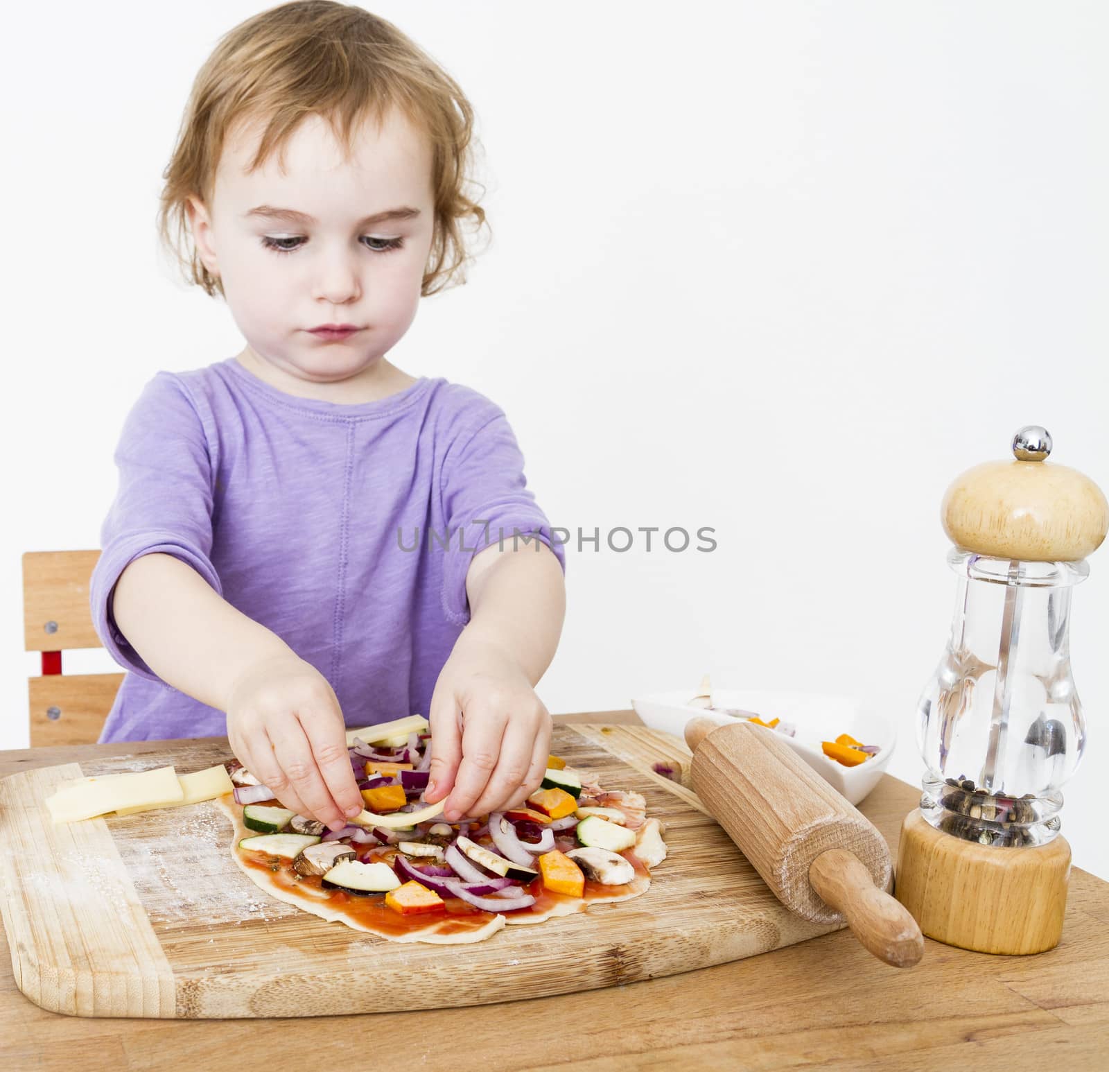 cute little girl preparing fresh pizza in neutral grey background