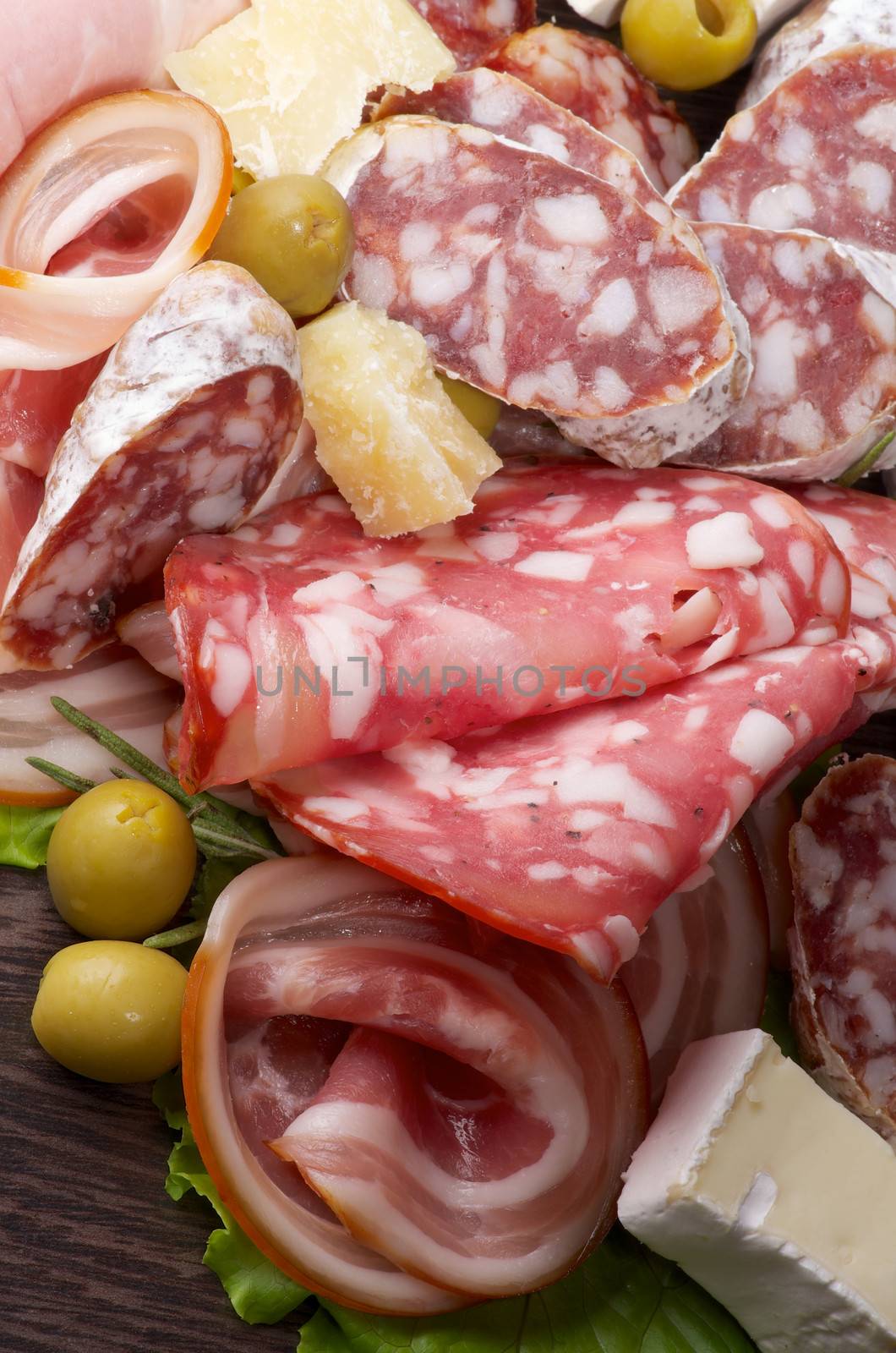 Delicatessen Cold Cuts with Smoked Ham, Pepperoni, Salami, Green Olives and Brie Cheese closeup on Dark Wooden background