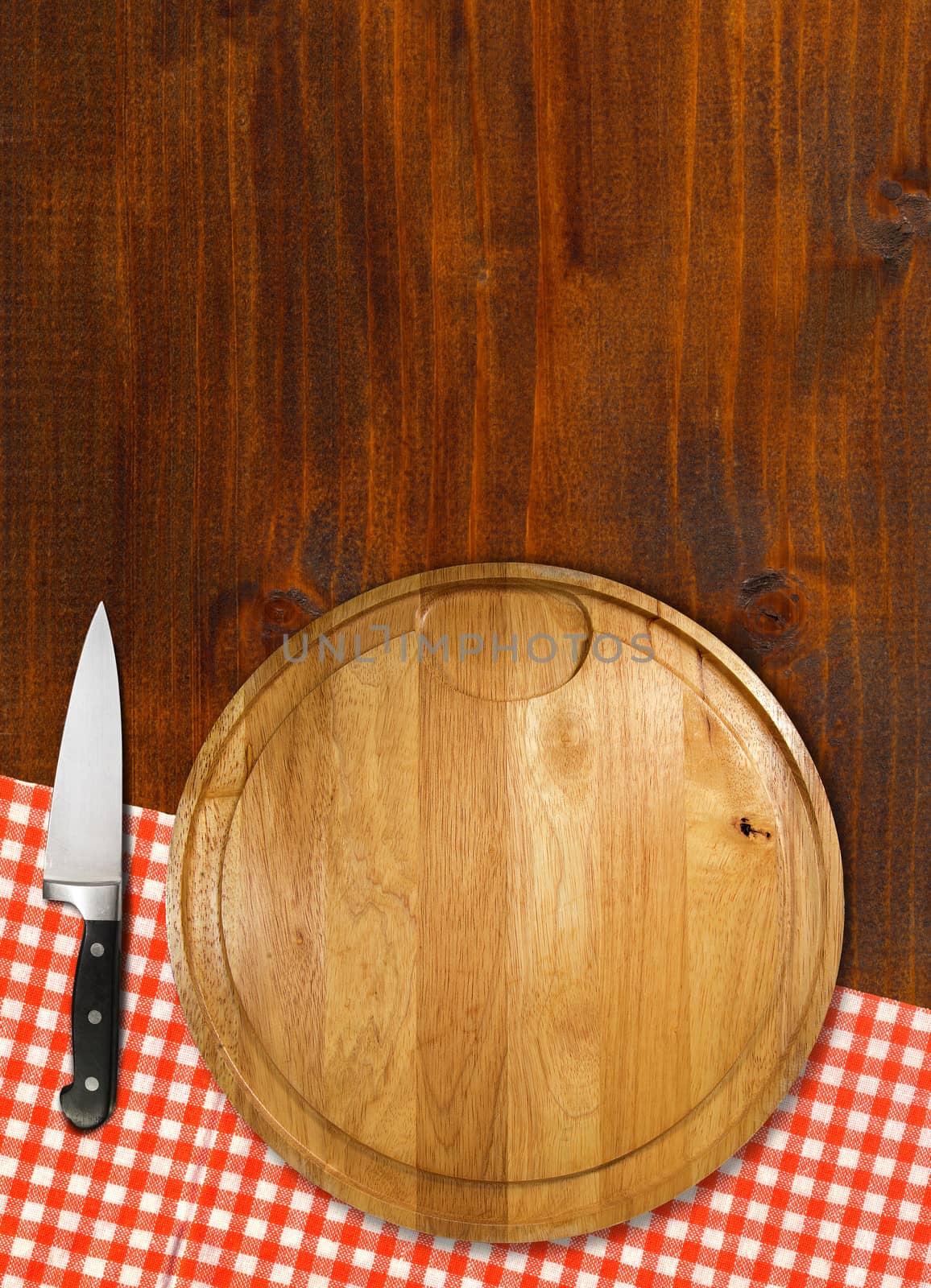 Round cutting board with red checked tablecloth and kitchen knife on brown wooden table