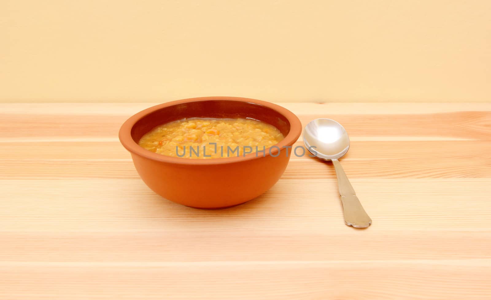 Bowl of vegetable soup with a spoon on a pine table with copy space