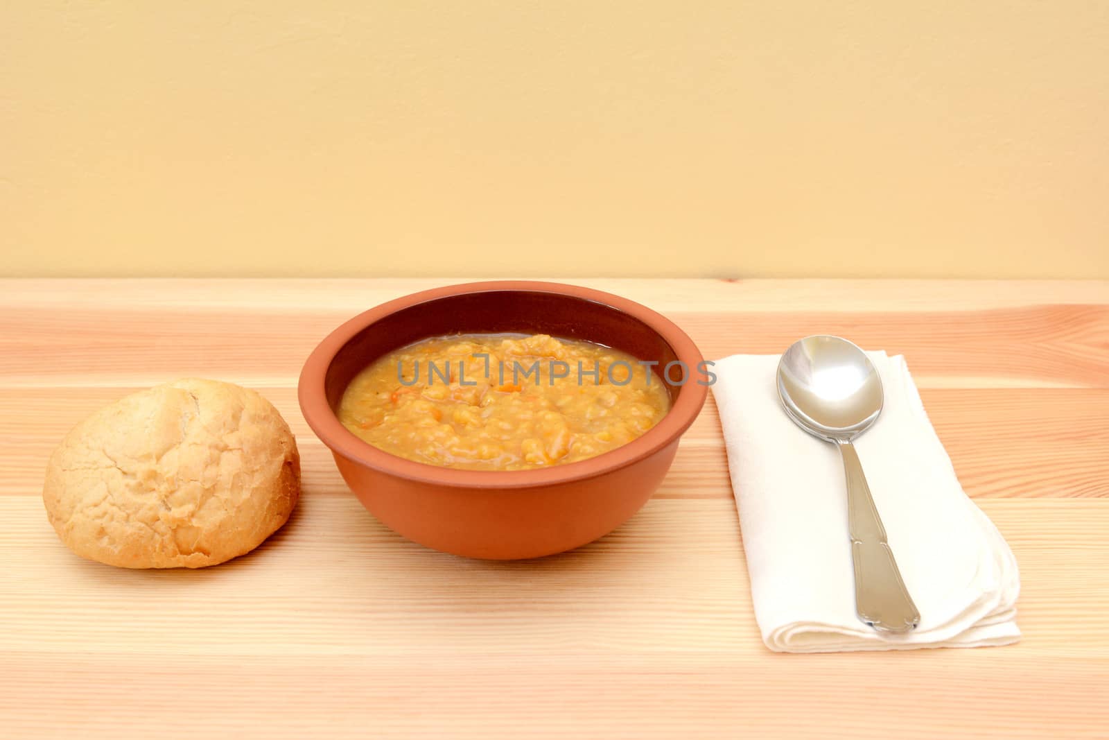 Vegetable soup in a bowl with crusty bread roll, spoon and linen napkin
