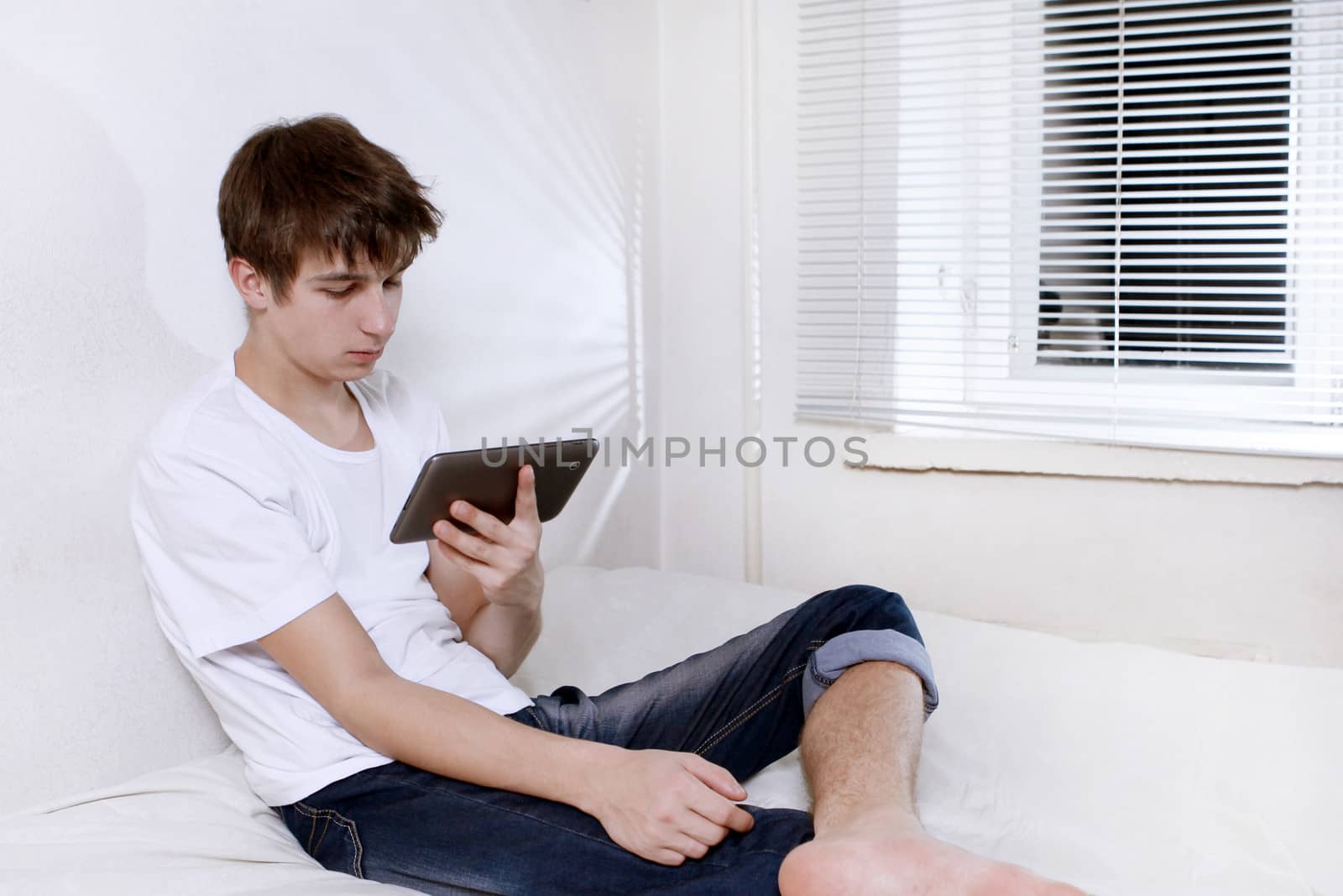 Sad and Tired Young Man with Tablet Computer sitting on the bed