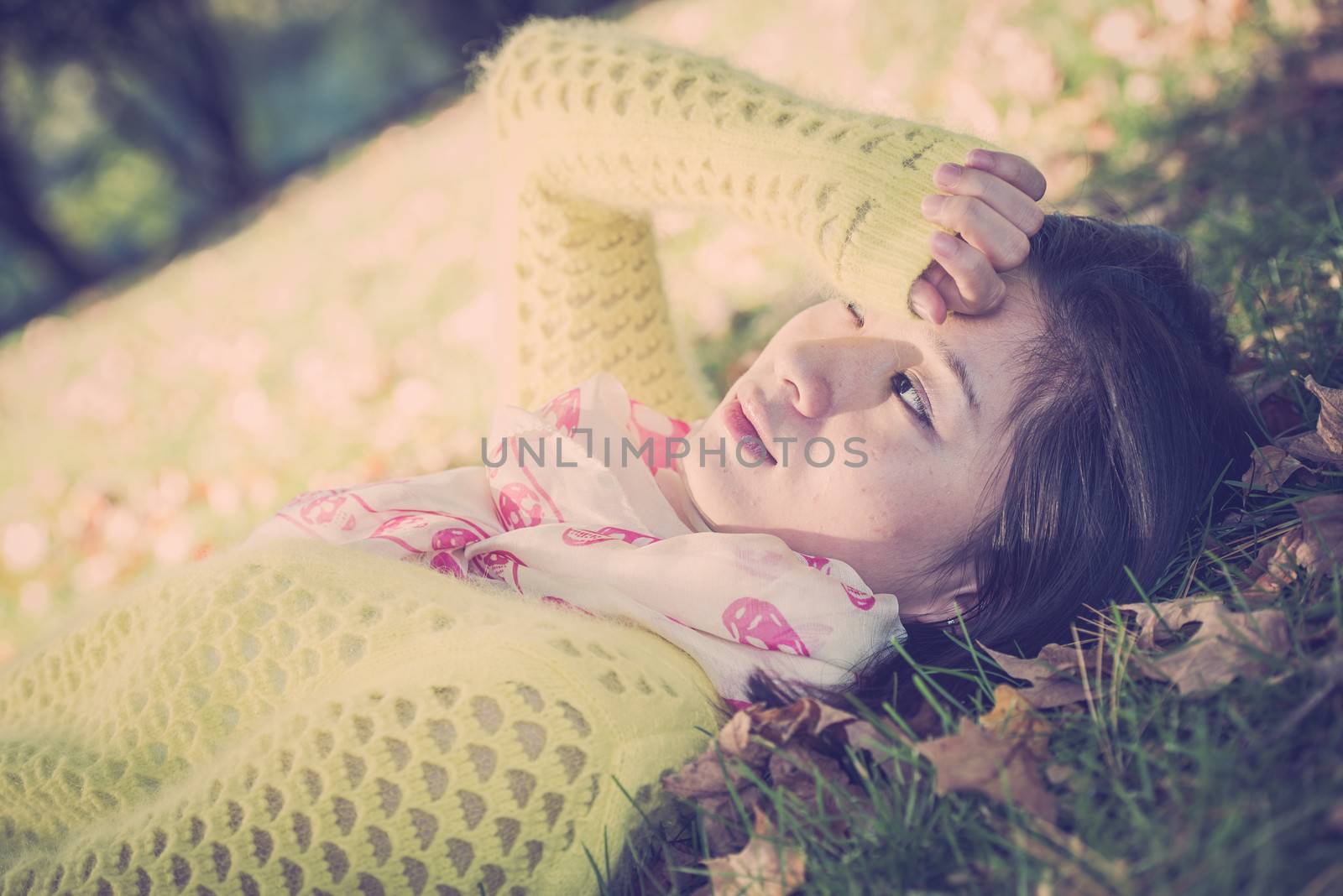 Young woman laying in grass with a bunch of fallen leafs, covering one eye