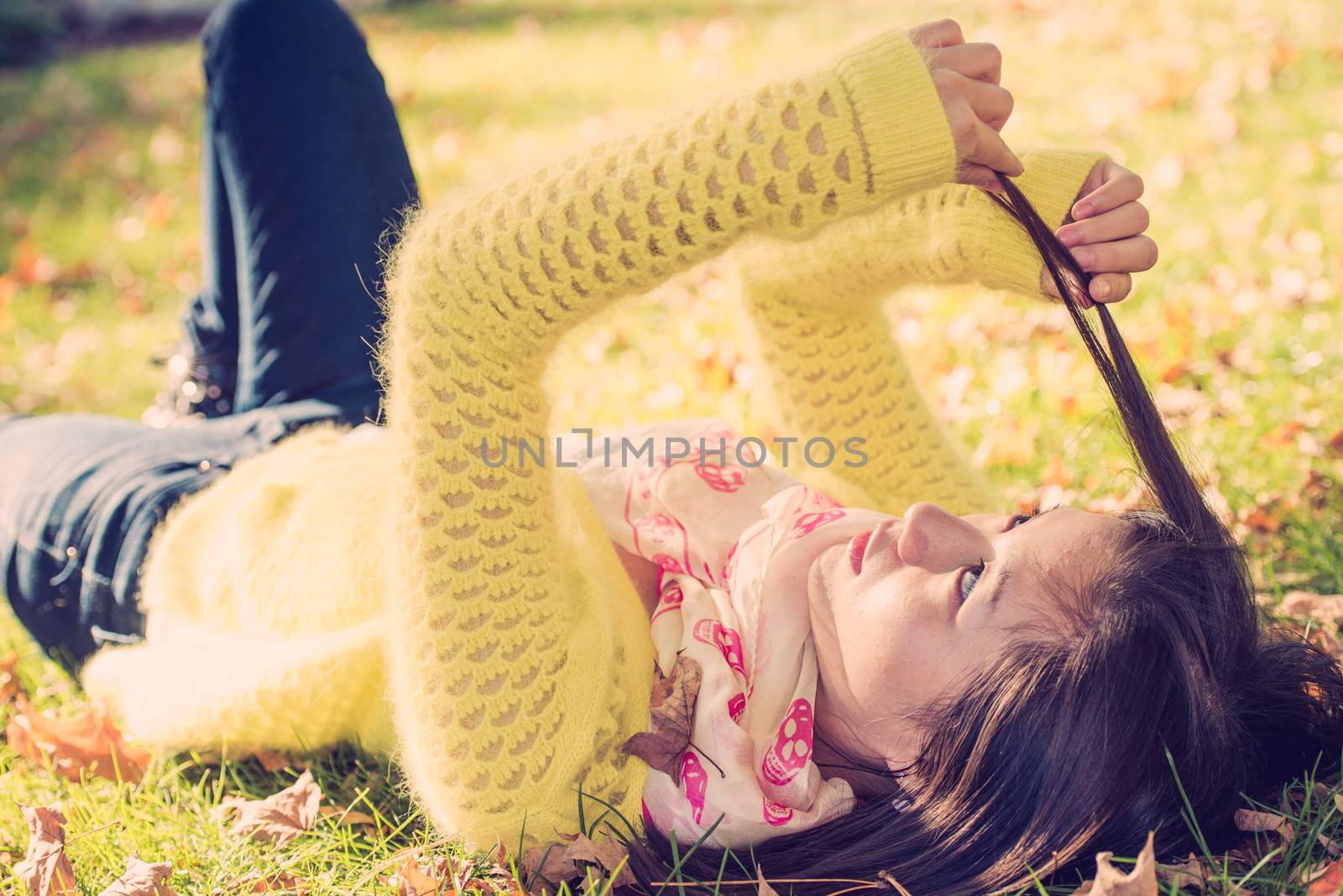 Young woman laying in grass with a bunch of fallen leafs playing with her hair