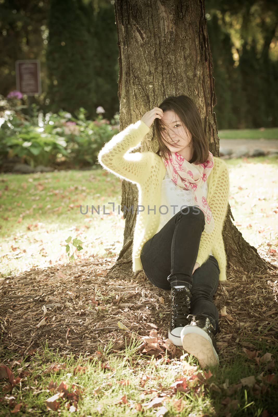 Portrait of happy looking woman sitting against a tree and brushing hair away from face