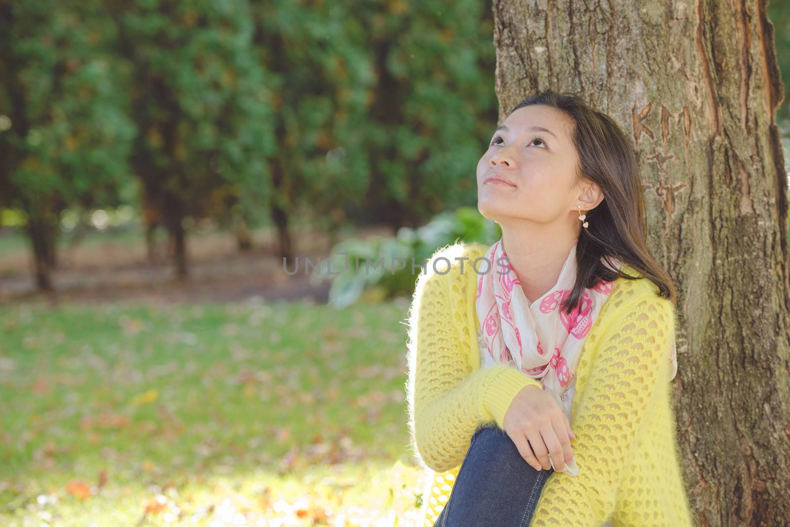 Portrait of happy looking woman sitting against a tree and looking upwards