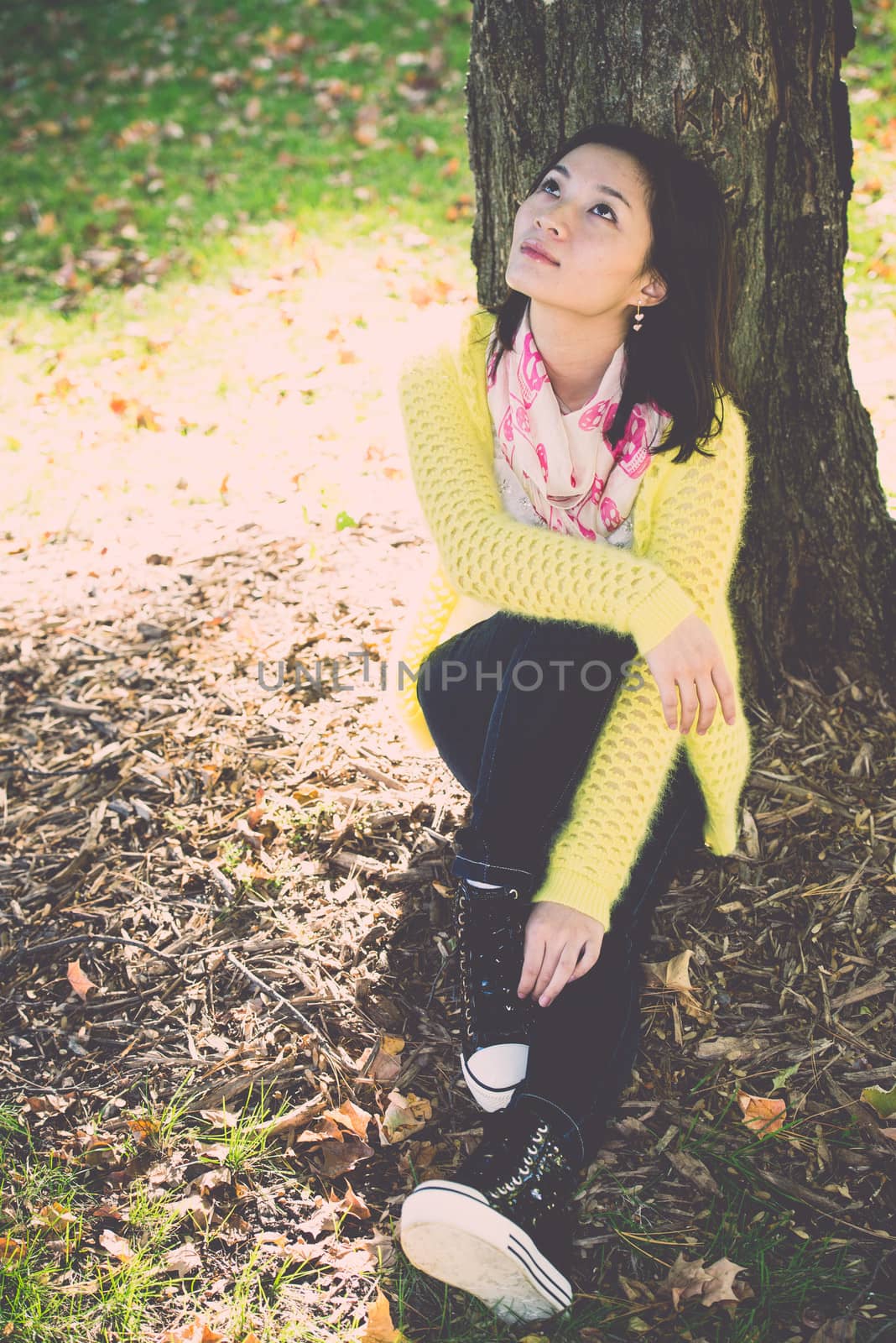 Portrait of happy looking woman sitting against a tree and looking upwards