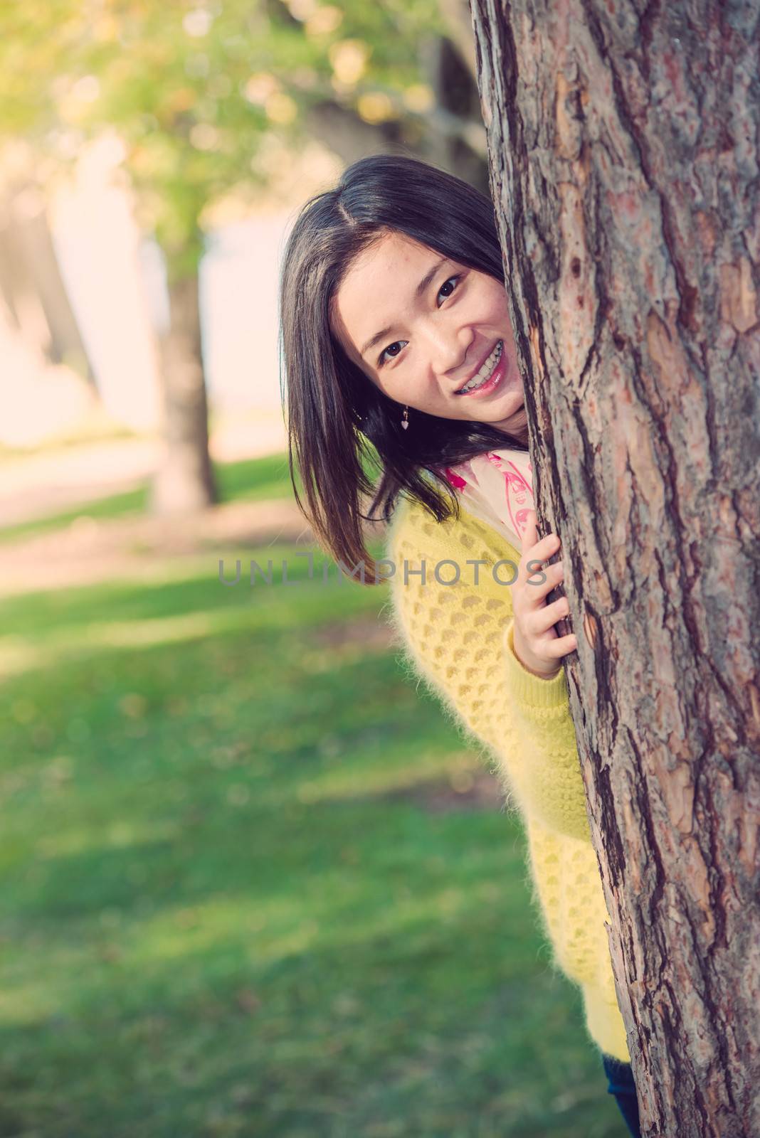 portrait of shy young woman peaking from behind a tree and smiling