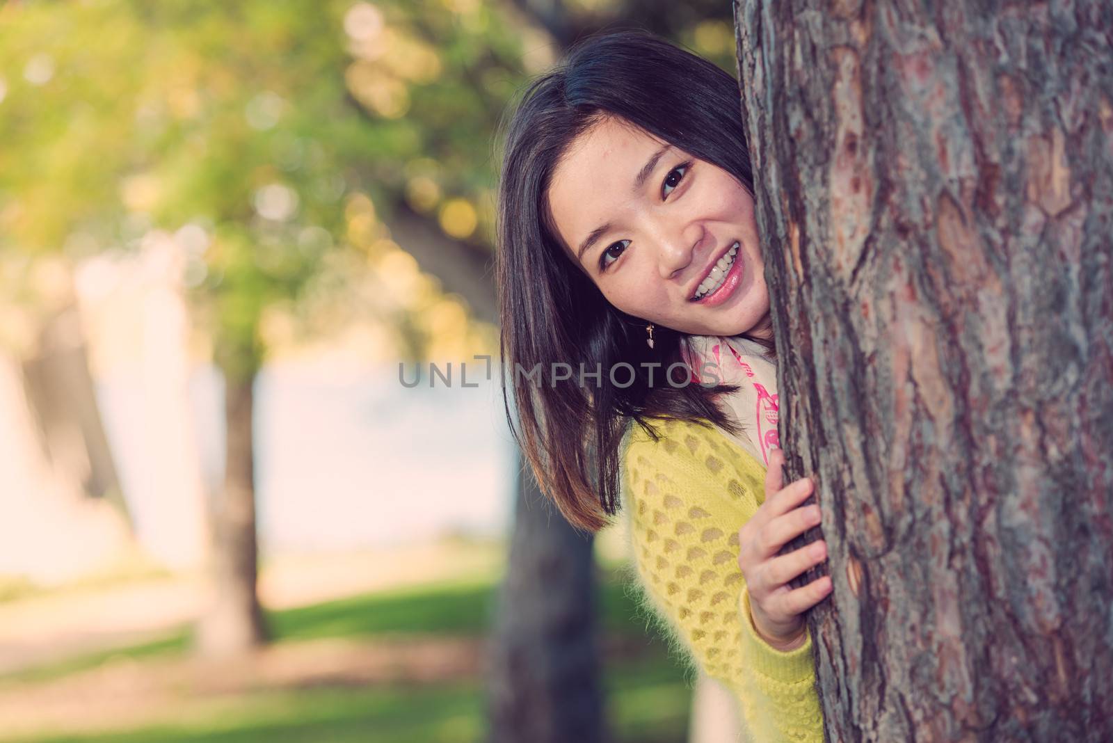 portrait of shy young woman peaking from behind a tree and smiling