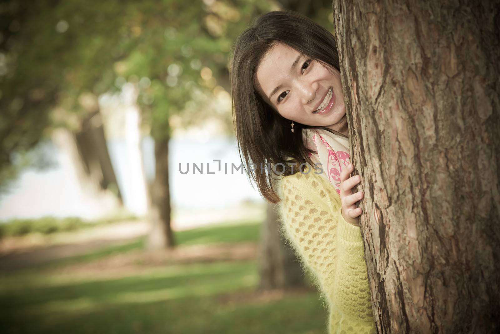 portrait of shy young woman peaking from behind a tree and smiling