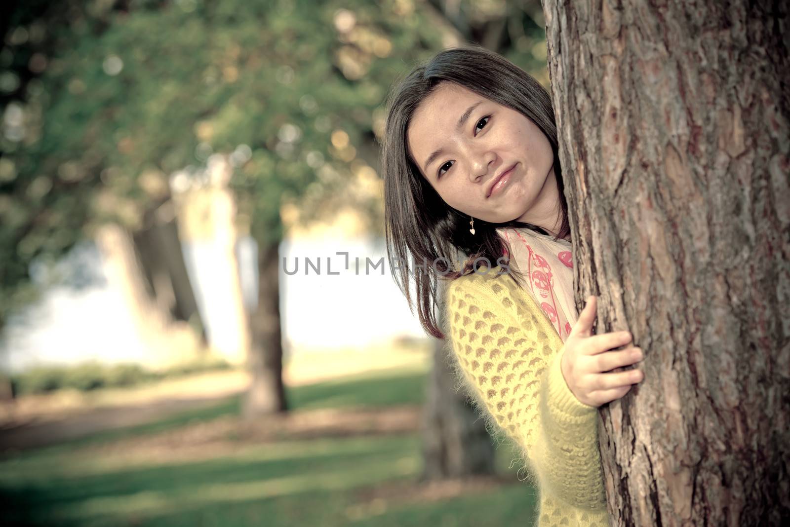 portrait of shy young woman peaking from behind a tree and smiling