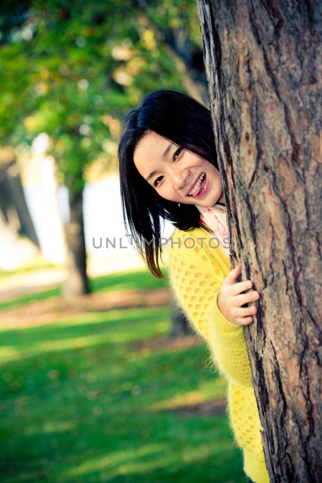 portrait of shy young woman peaking from behind a tree and sticking out her tougue