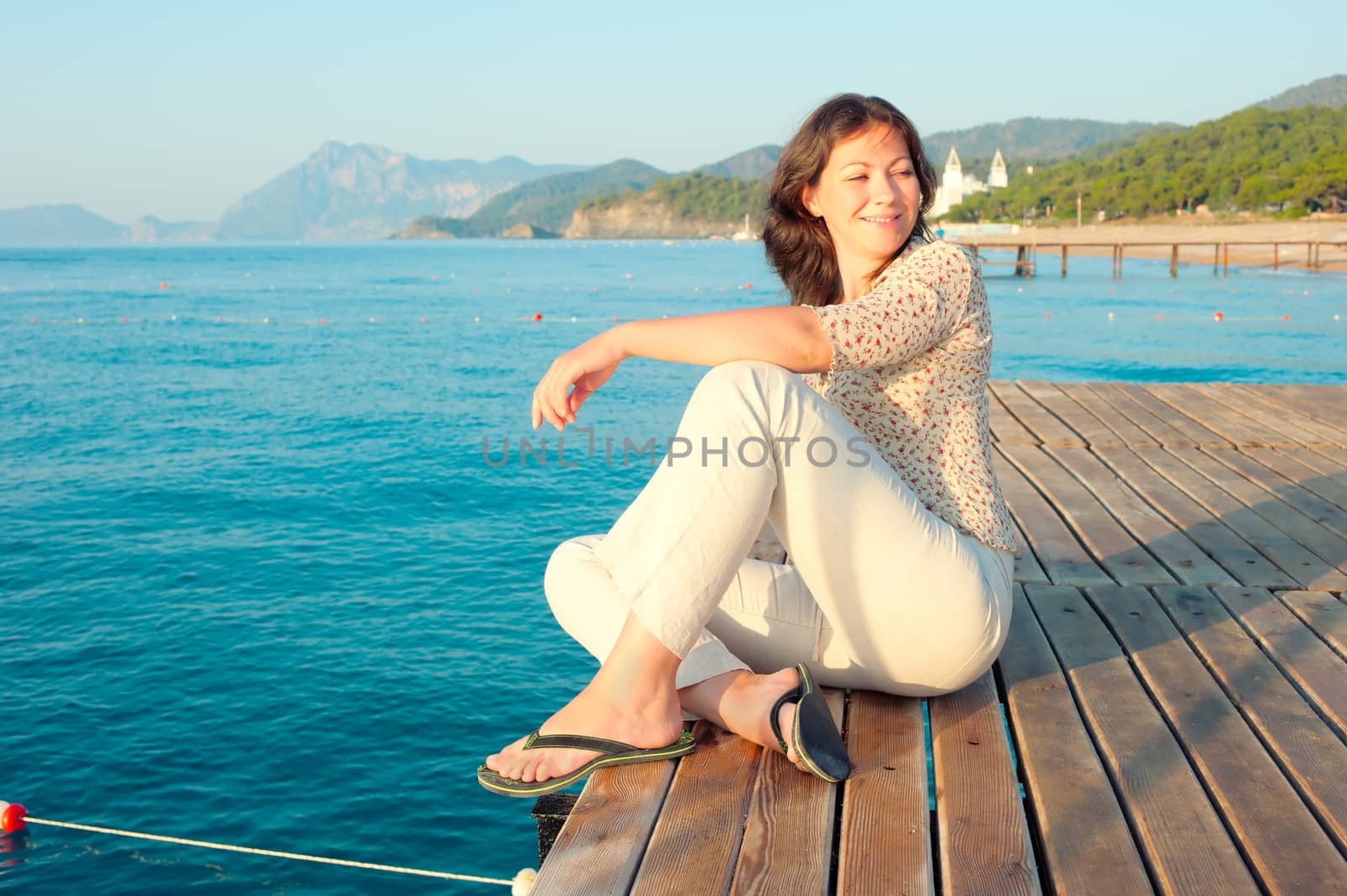 Young girl is resting on a wooden pier near the sea by kosmsos111
