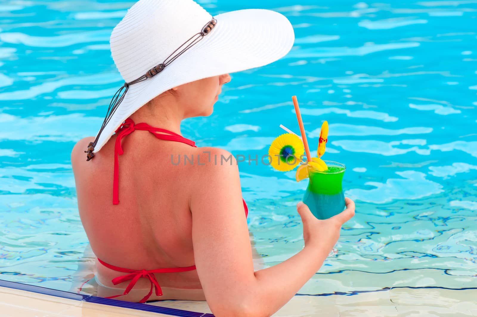 A girl in a white wide-brimmed hat with a cocktail in the pool by kosmsos111