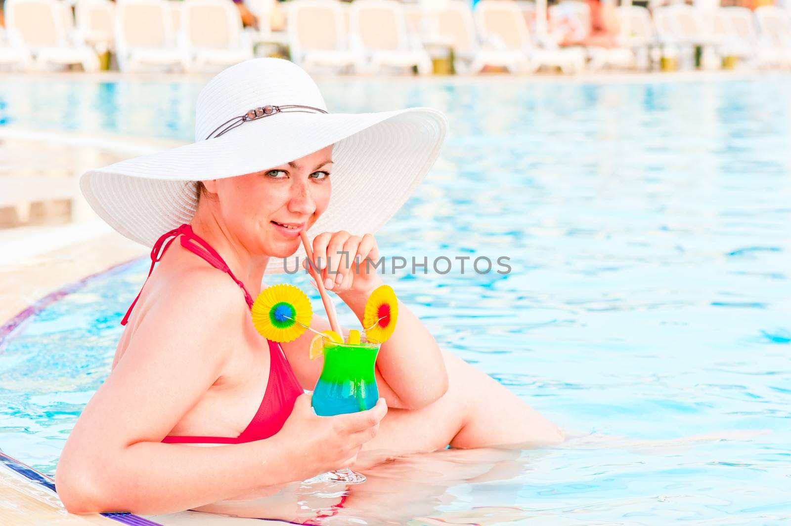 young female trying to drink in a glass sitting in the pool