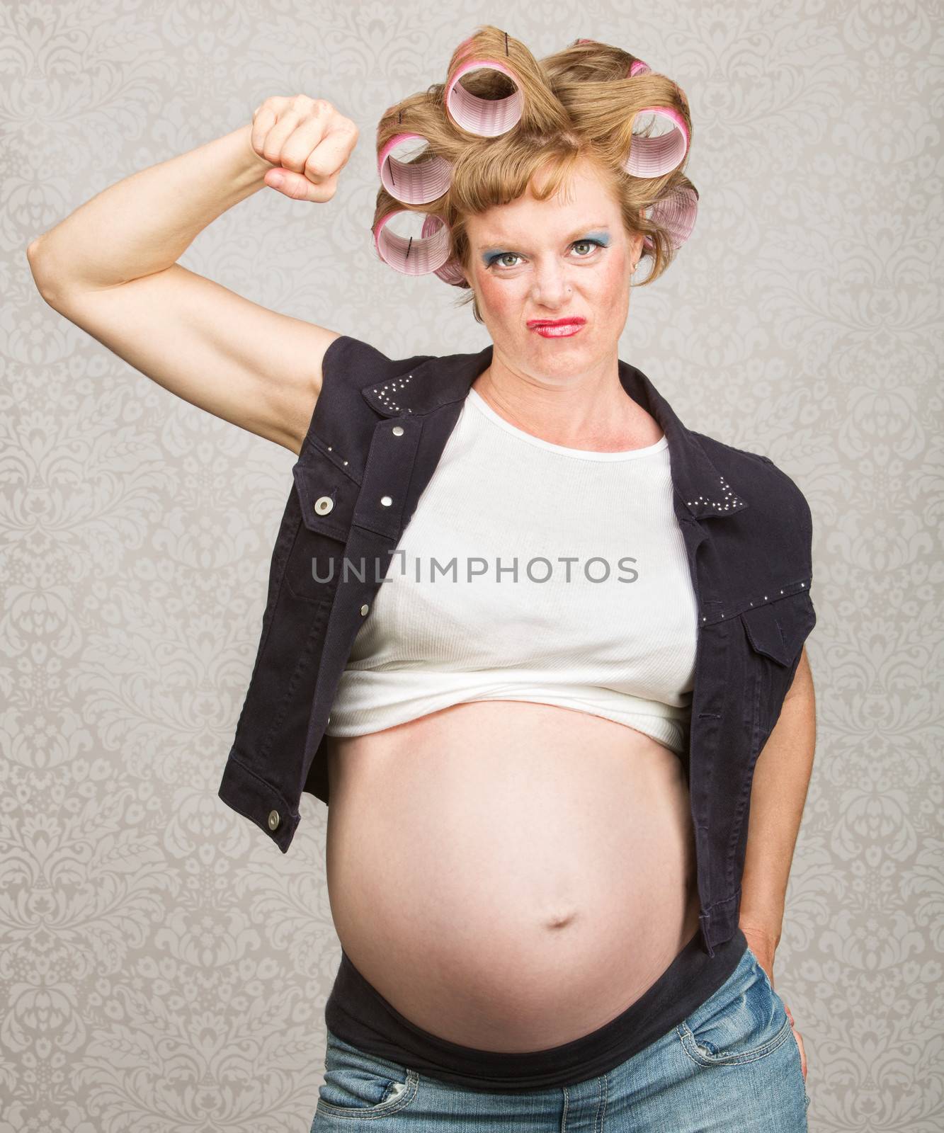 Young pregnant woman in curlers flexing her biceps