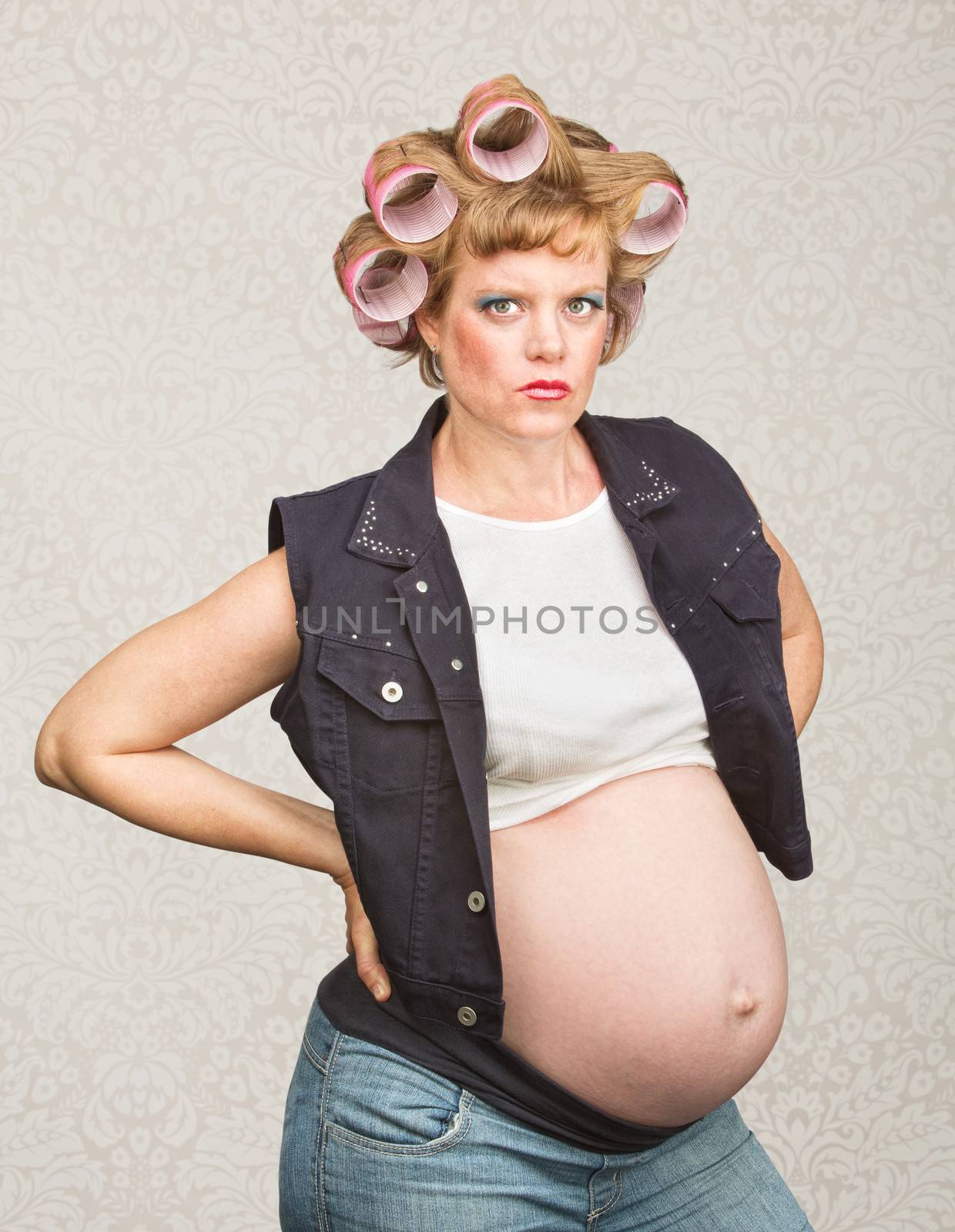 Serious pregnant female in curlers with hands on hips