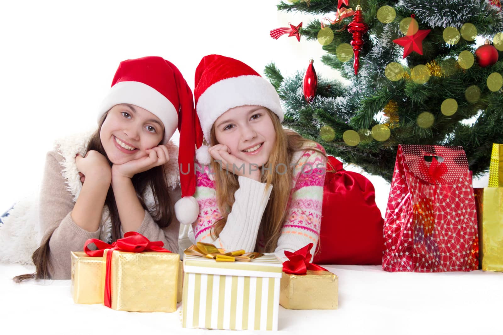 Two smiling sisters in Santa hats lying under Christmas tree