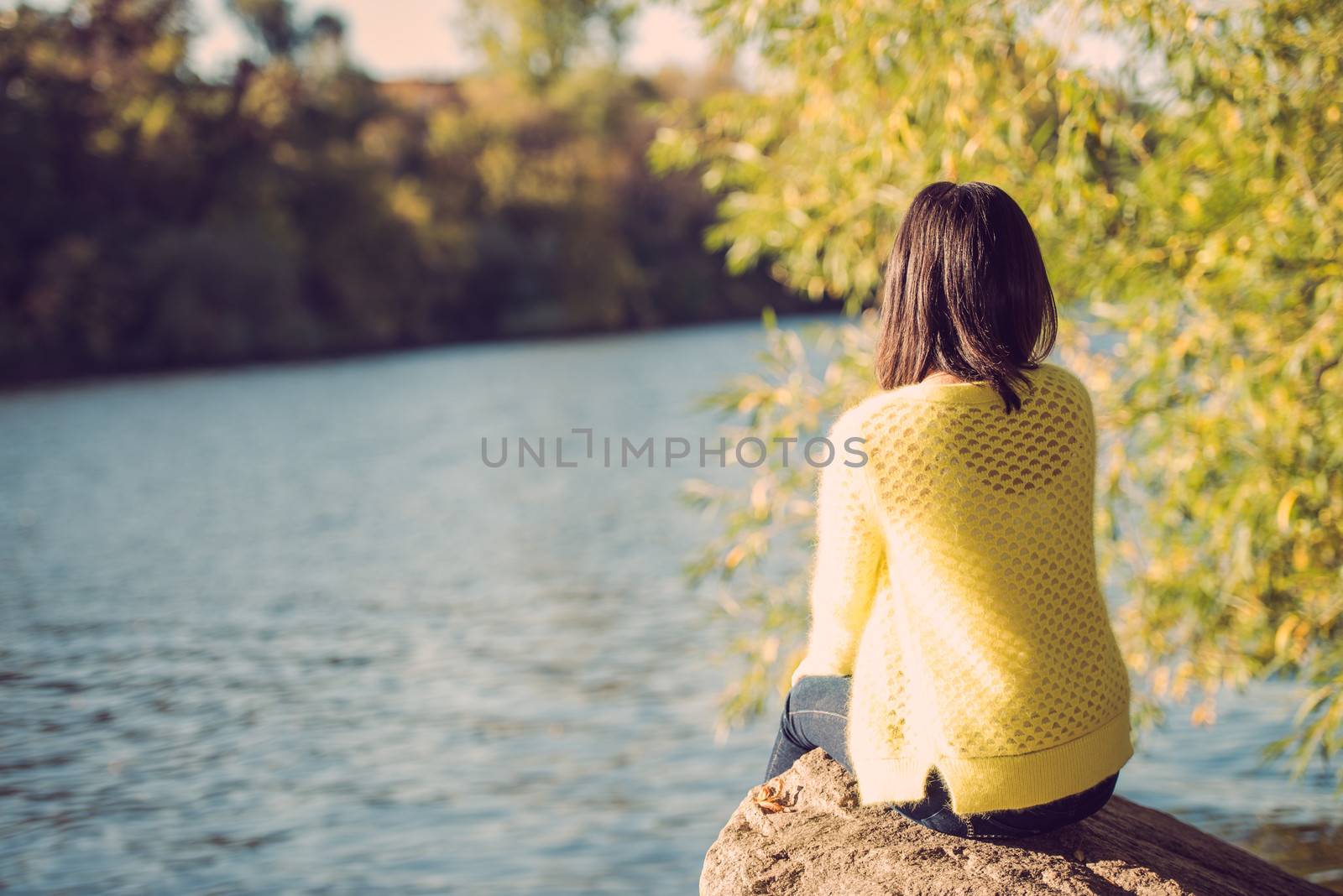 Attractive lonely young woman sitting on a rock next to river looking upset