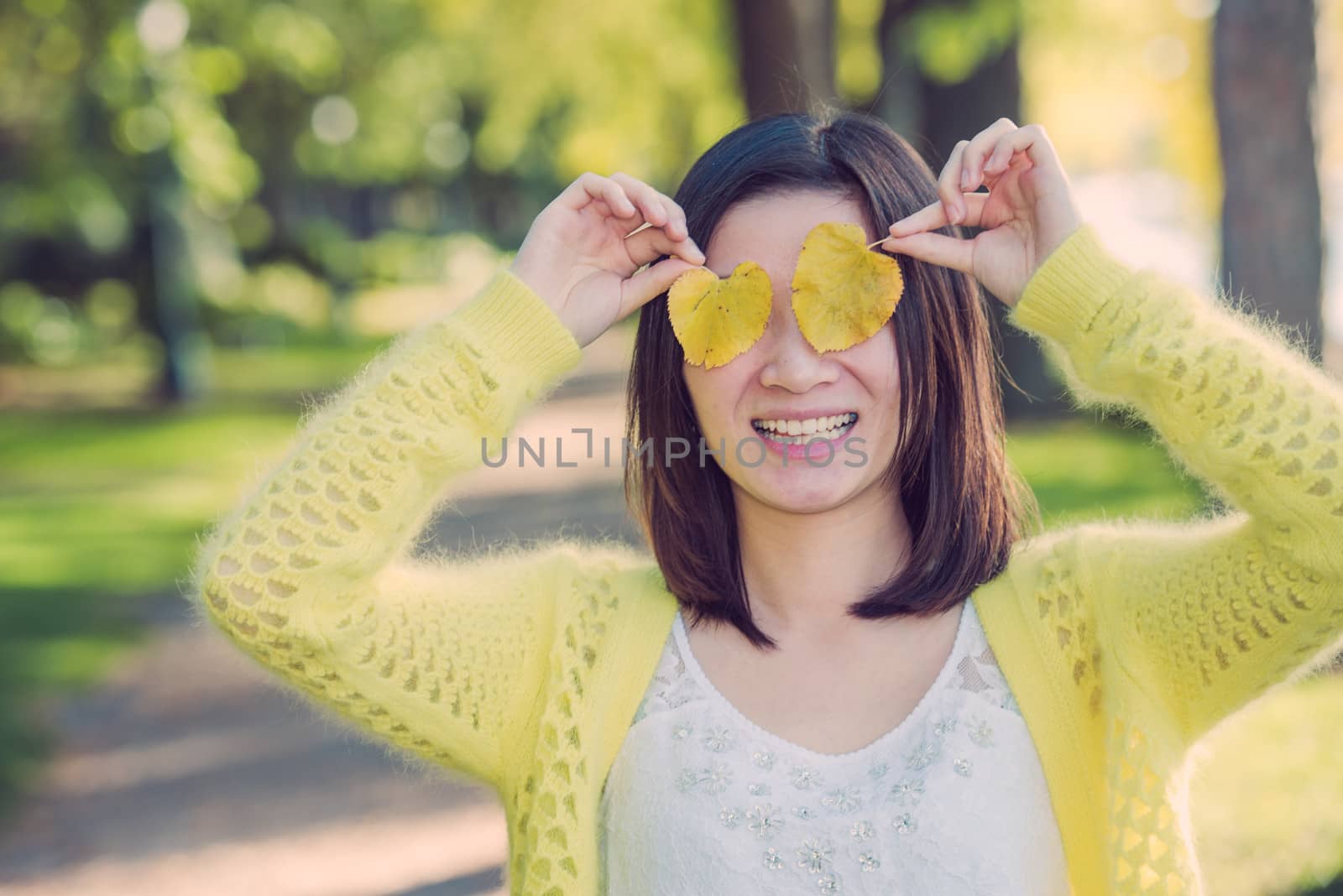 Portrait of cute young girl covering eyes with two leafs at an end of a park road