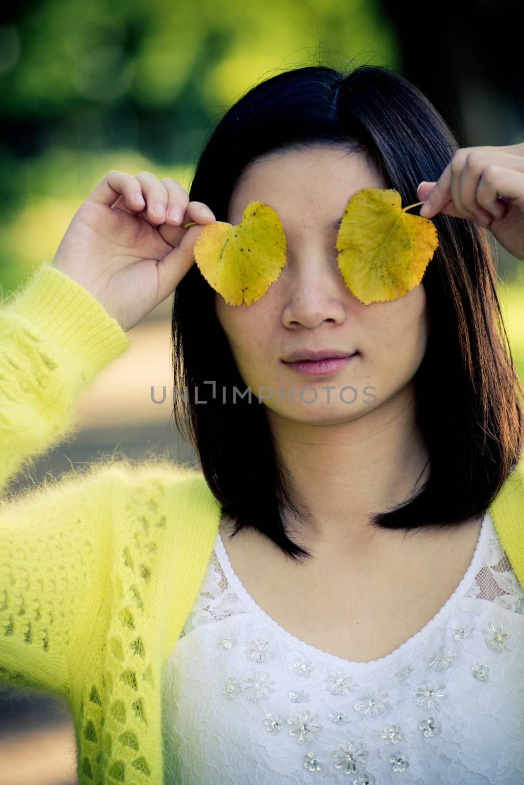 Portrait of cute young girl covering eyes with two leafs at an end of a park road