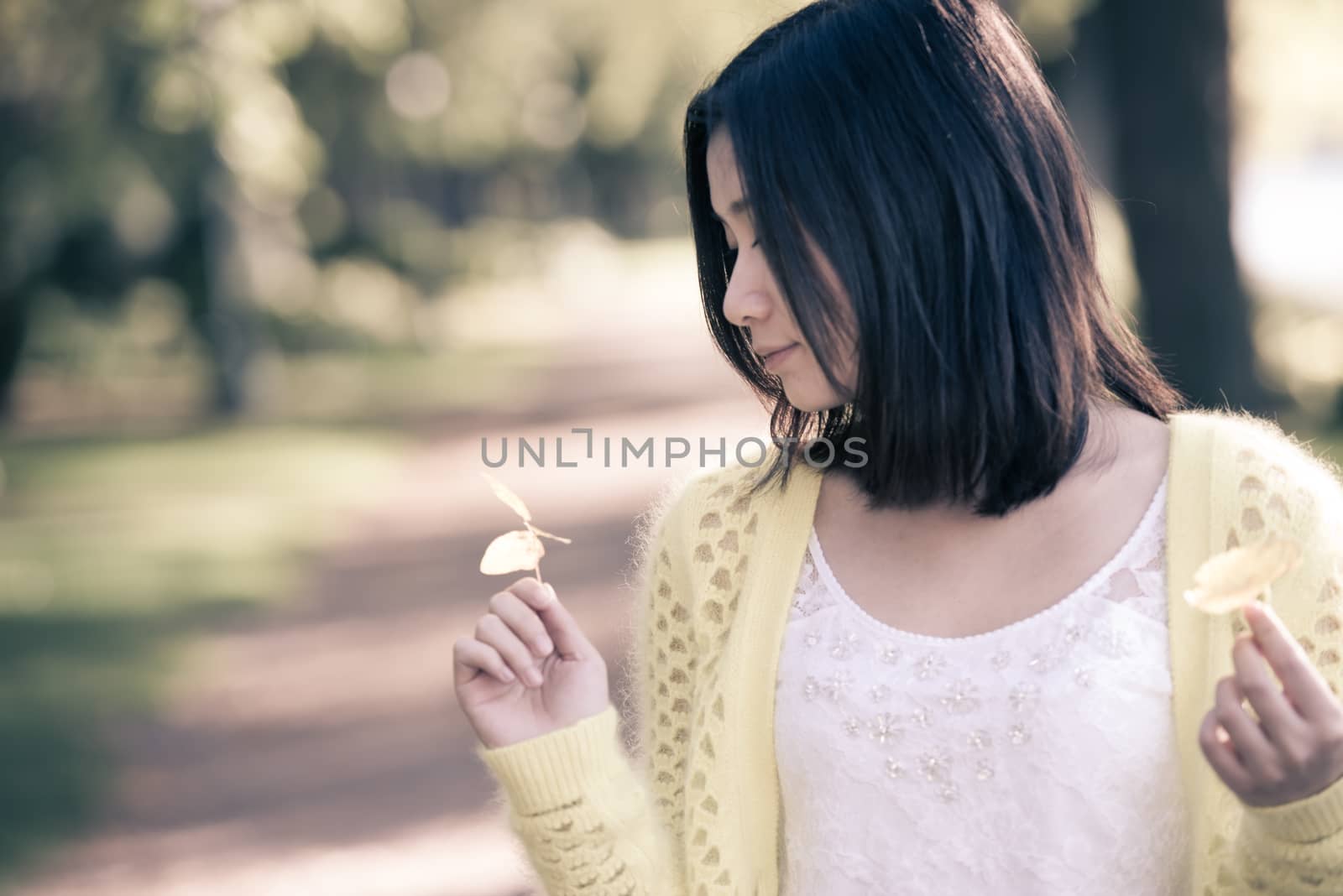 Cute young girl holding a handful of leafs at the end of a park road