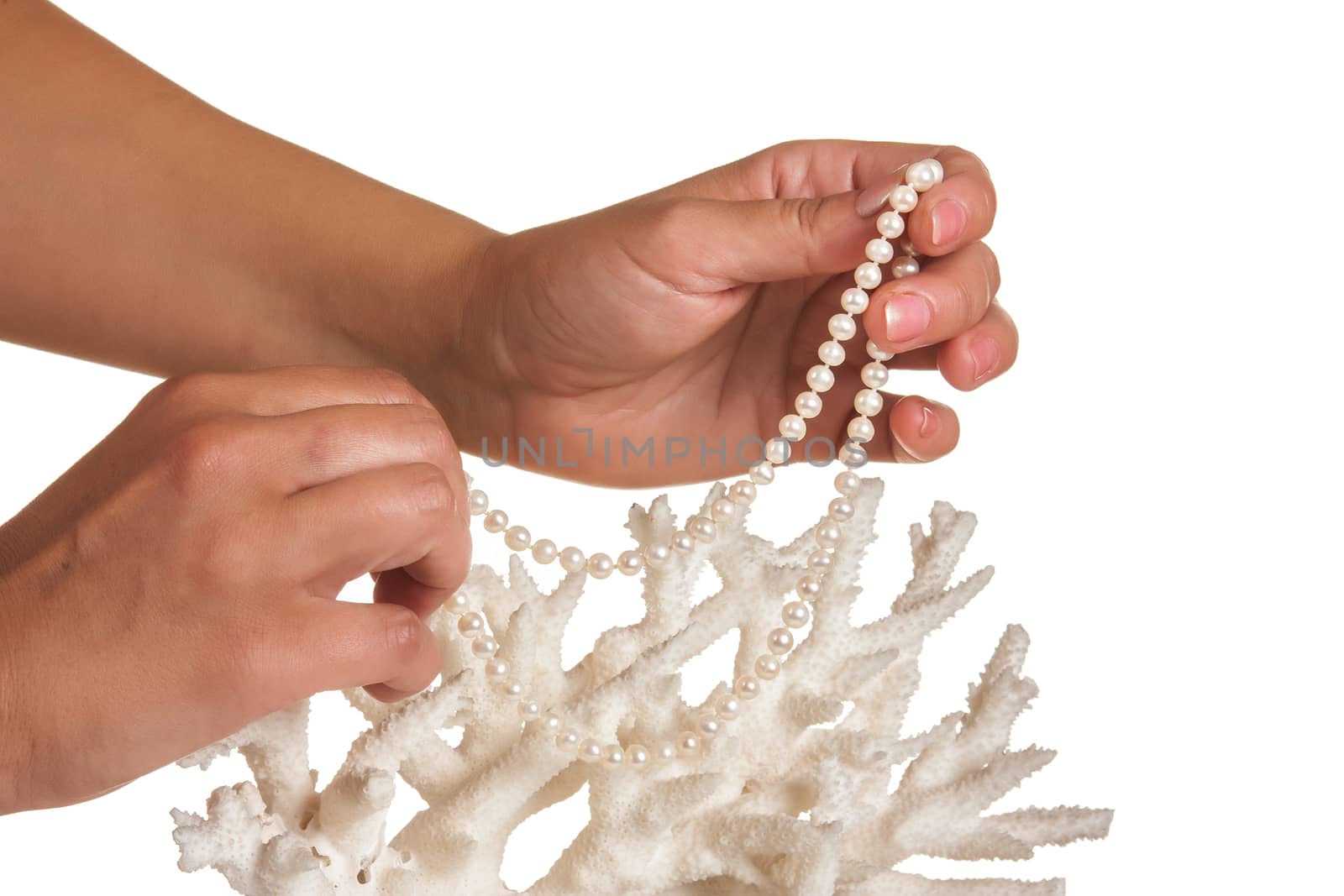 a pearl necklace in her hands against the backdrop of coral isolated on a white background